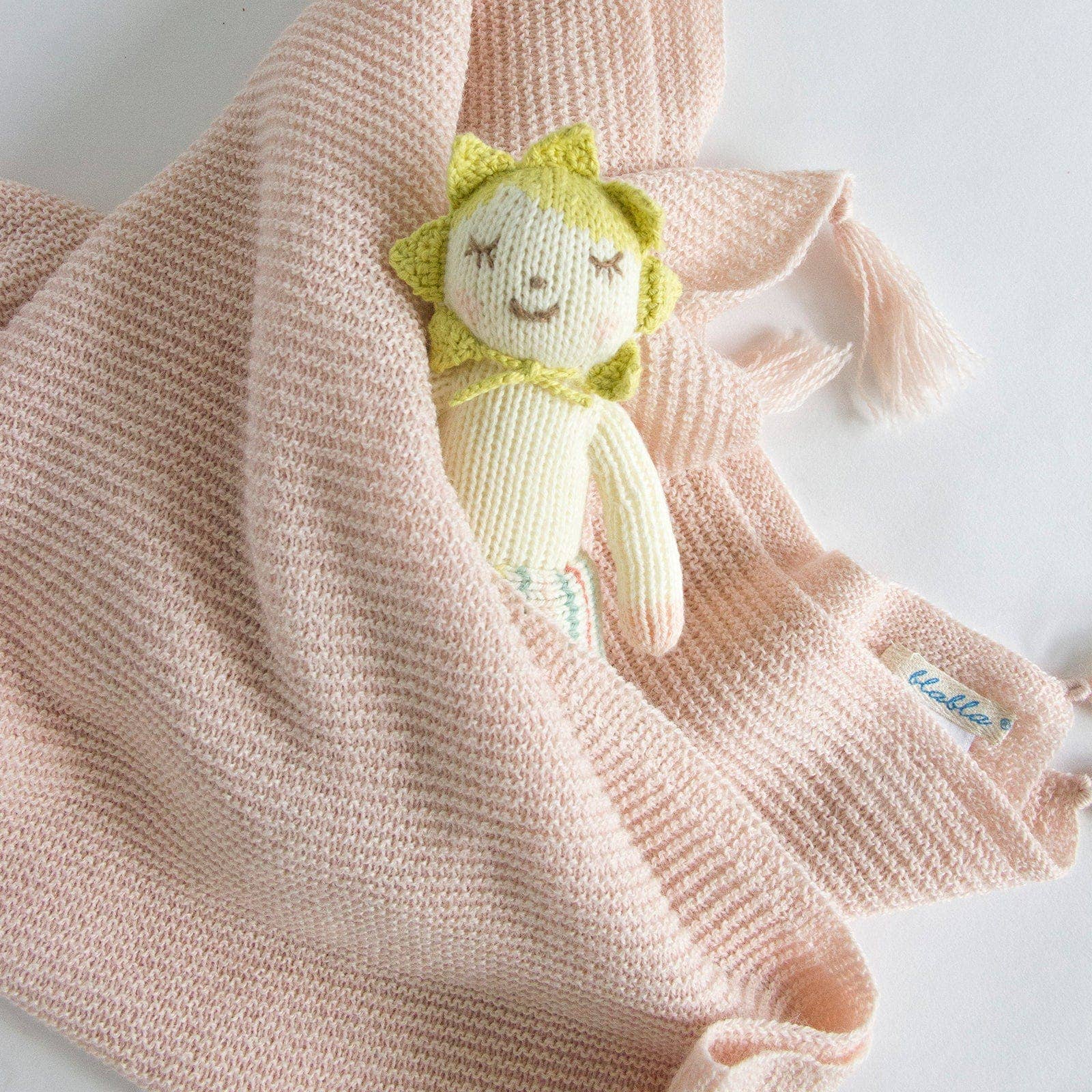 Knitted sun-shaped toy with tassels on a soft pink blanket