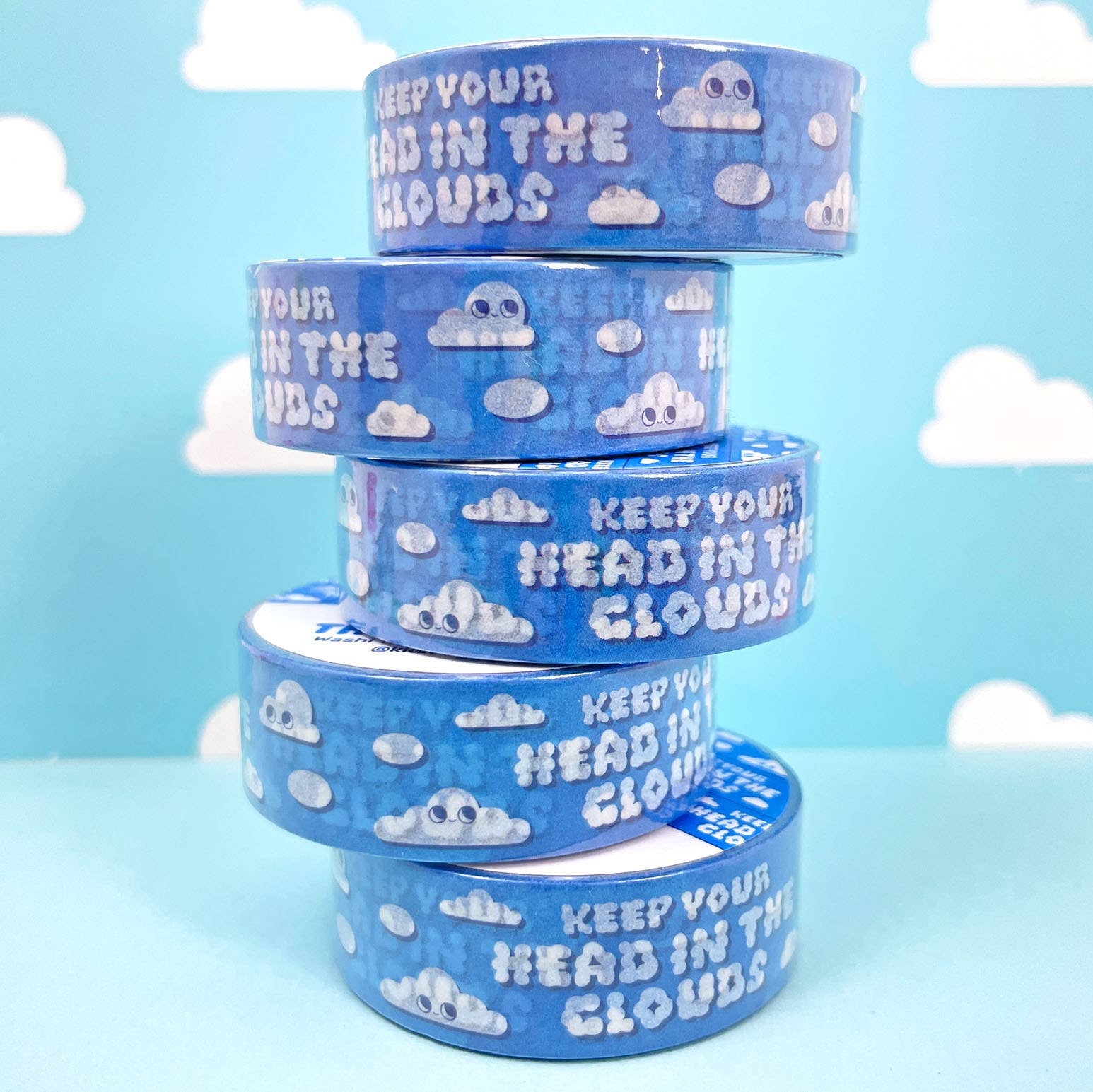 Stack of blue washi tape rolls with cloud designs and text on a light blue background with white clouds.