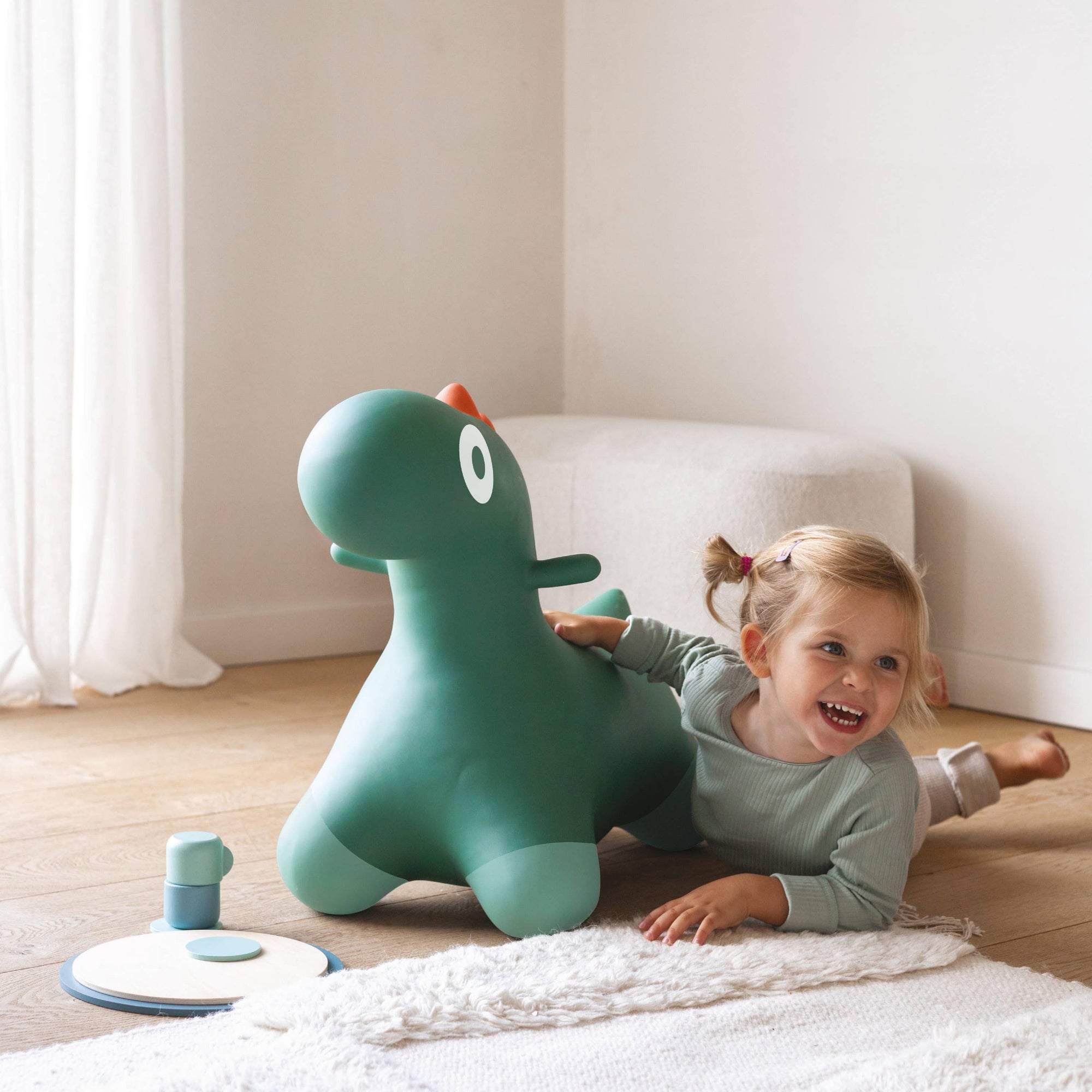 Child playing with a green dinosaur-shaped inflatable toy on a light wooden floor.