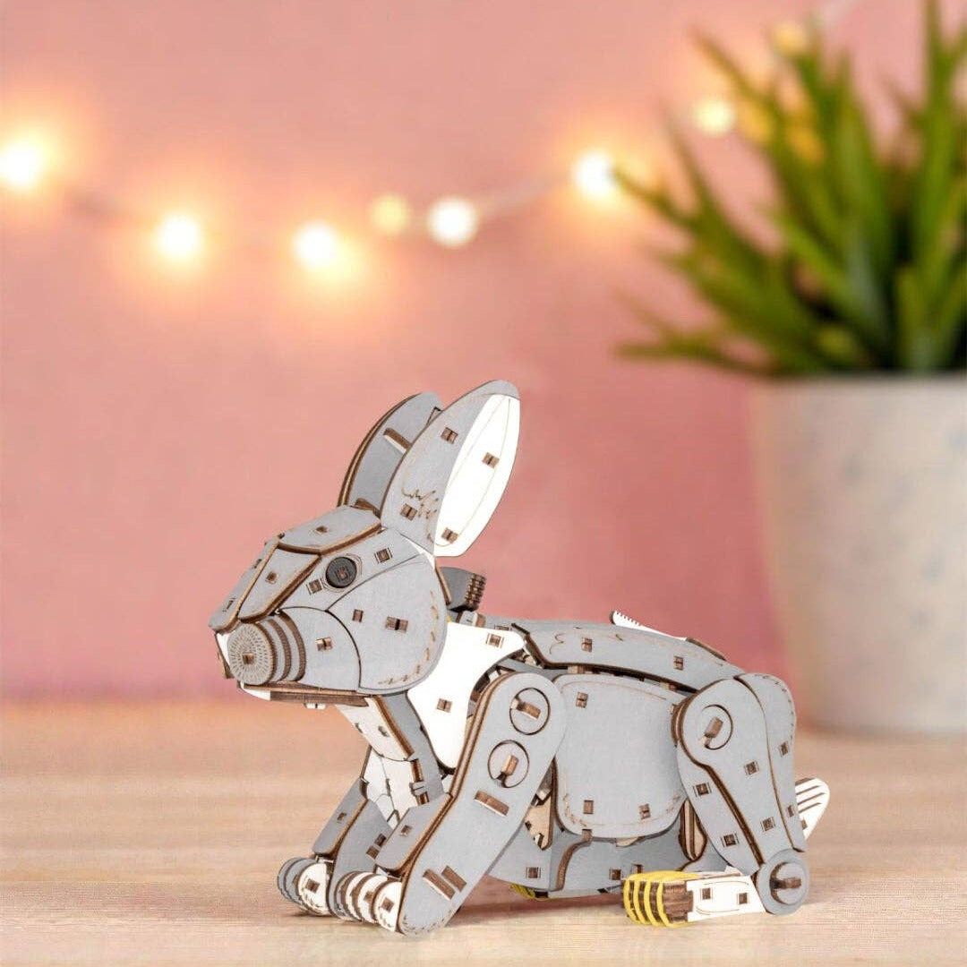 Mechanical rabbit model on a wooden surface with a pink background and string lights.