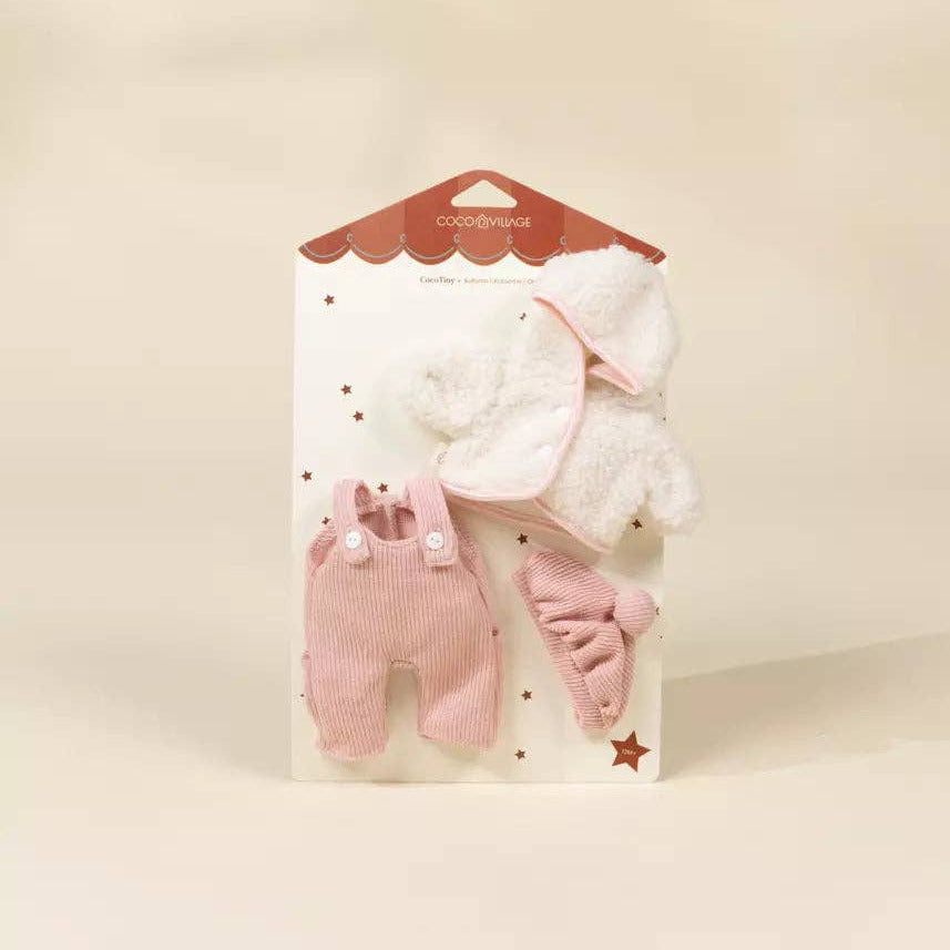A three-piece baby accessory set in pink and white, packaged on a white card with a brown scalloped header. The set includes a pink corduroy baby romper, a white plush hat, and a pink bootie, displayed against a warm beige background.