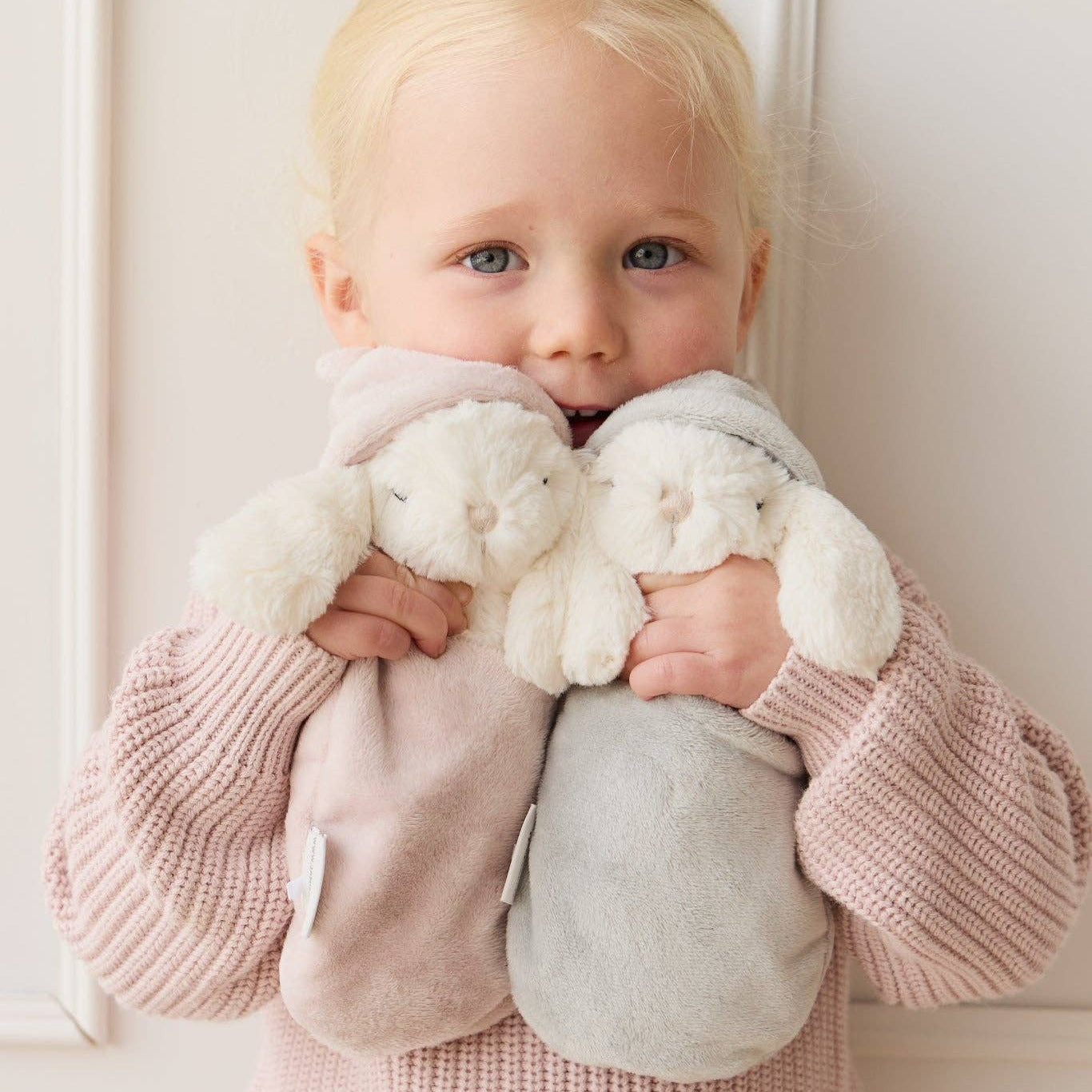 Child holding two plush toys against a white background