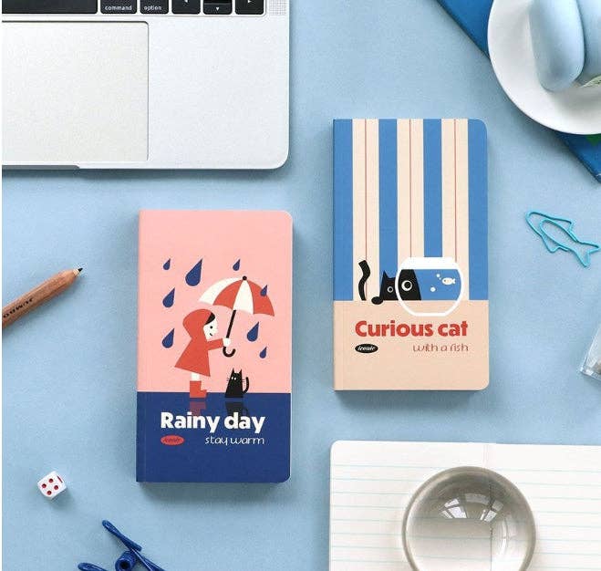 Two small notebooks with colorful covers on a light blue surface with office supplies.
