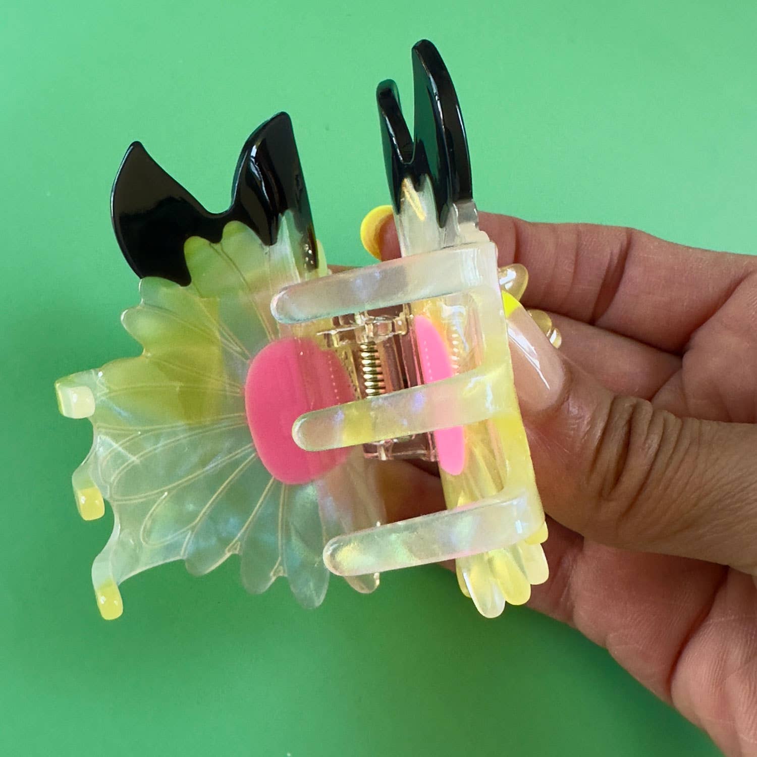 Hand holding a colorful hair clip against a green background