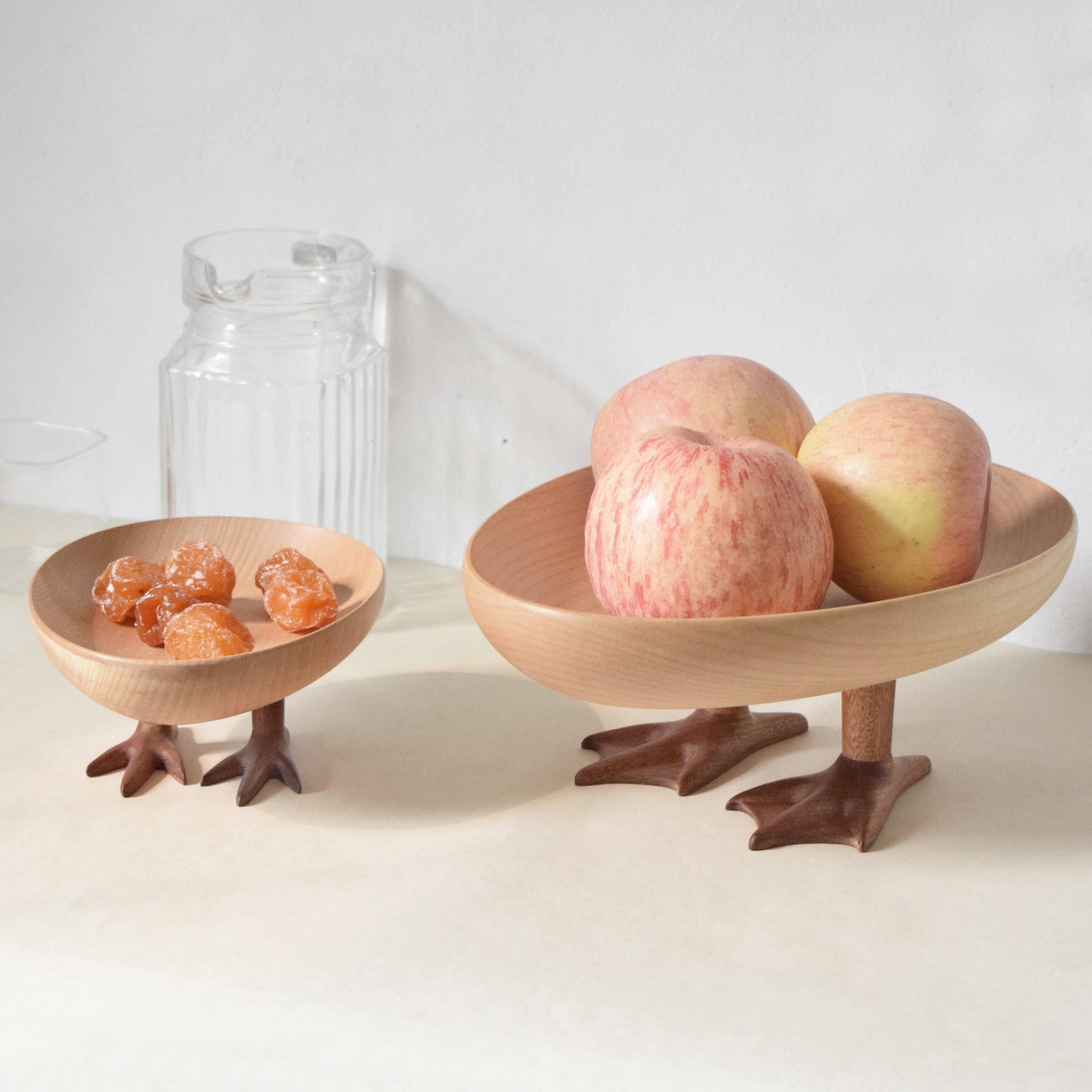 Wooden bowl with bird-like feet holding apples on a white surface