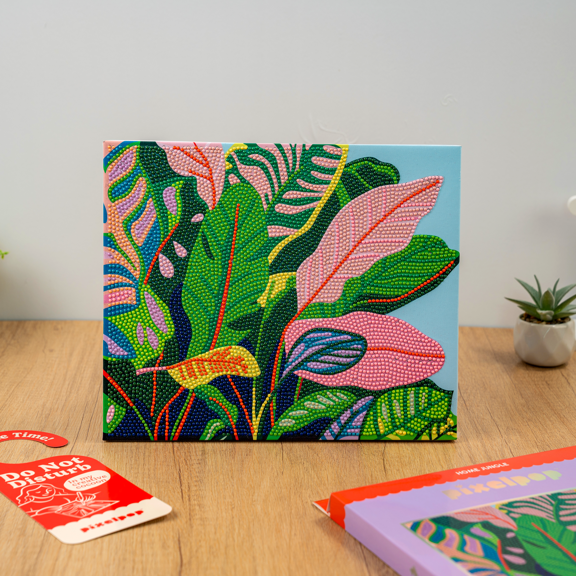 Colorful leaf-patterned board game box on a wooden surface with a plant in the background