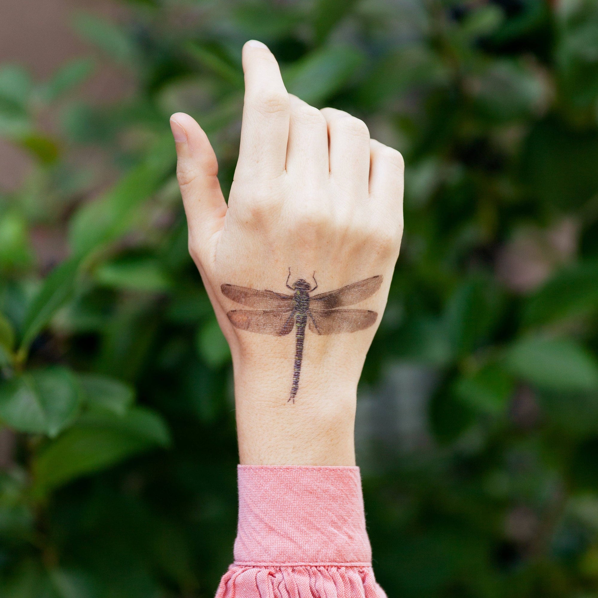 Hand with a dragonfly tattoo against a blurred green background