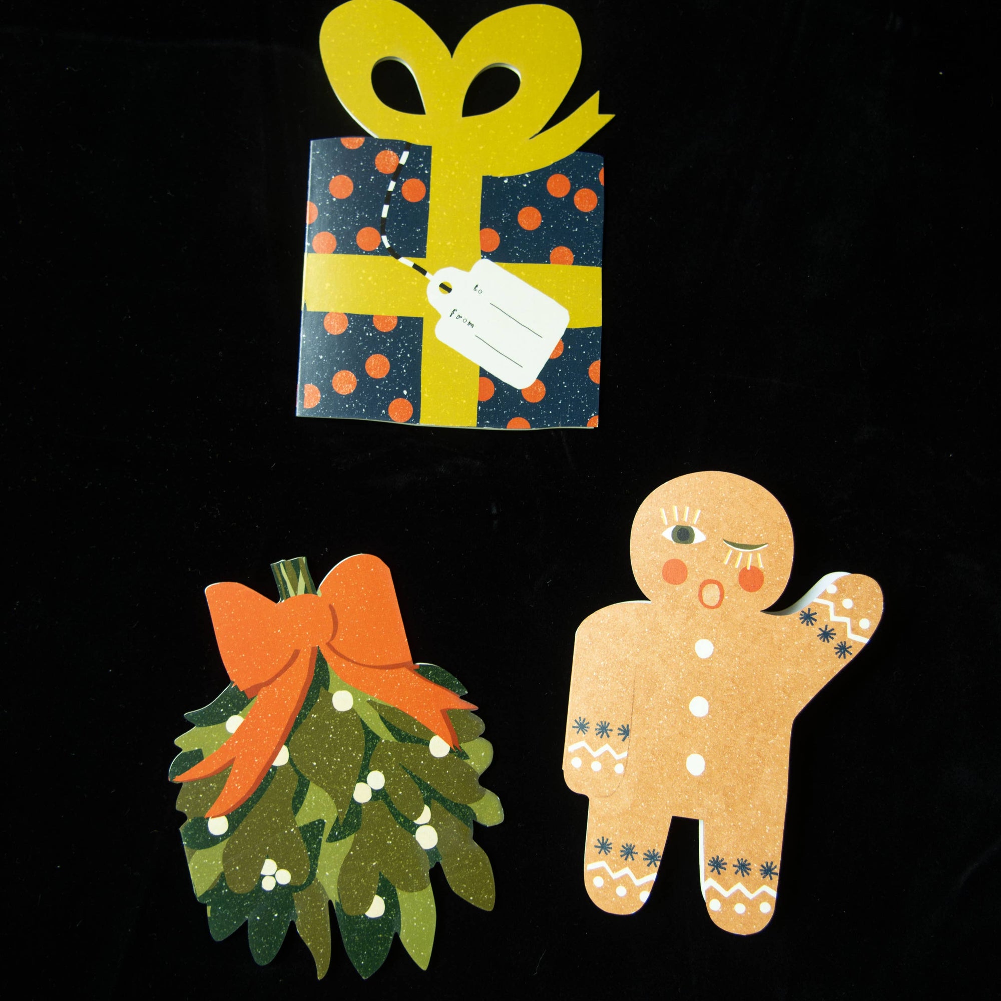 Decorative cutouts of a gift, gingerbread man, and wreath on a black background