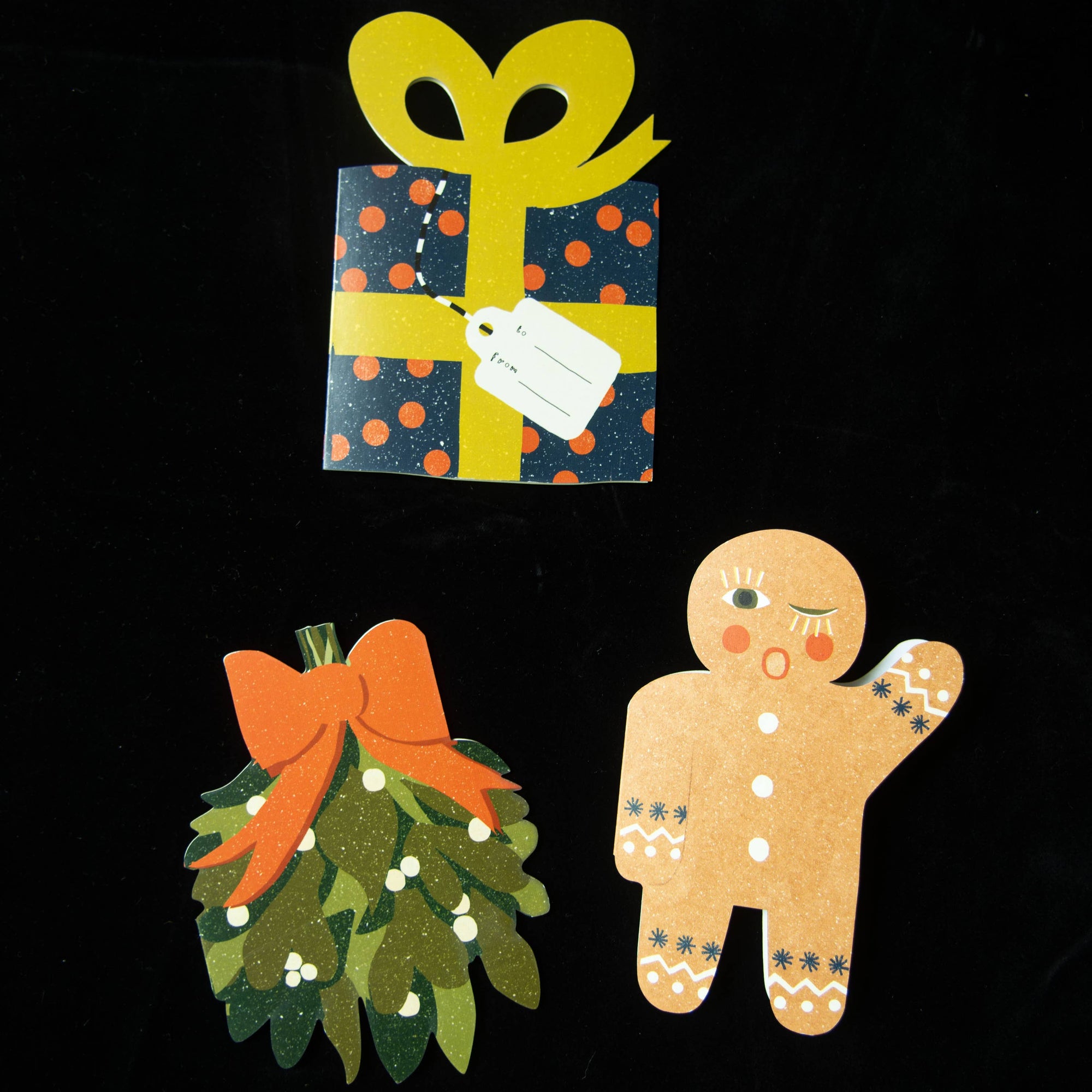 Decorative cutouts of a gift, gingerbread man, and wreath on a black background