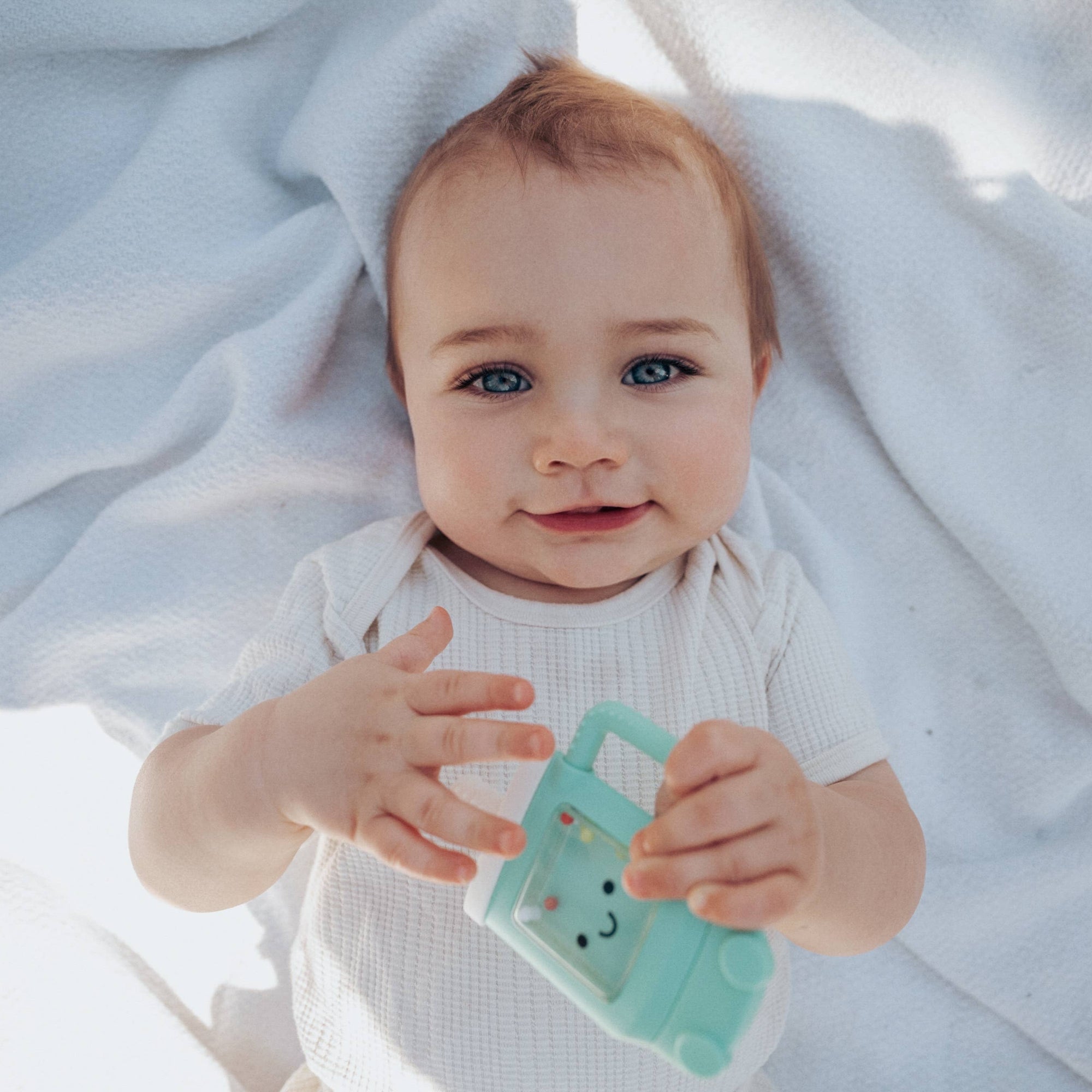 Baby holding a green toy with a bunny design on a white blanket
