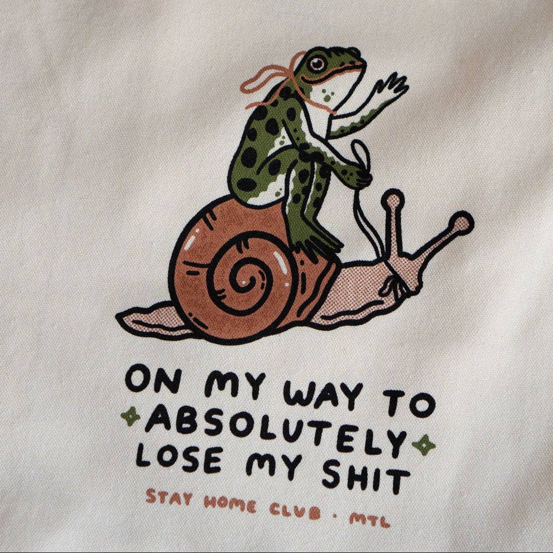Tote bag with a snail and frog illustration and humorous text on a white background