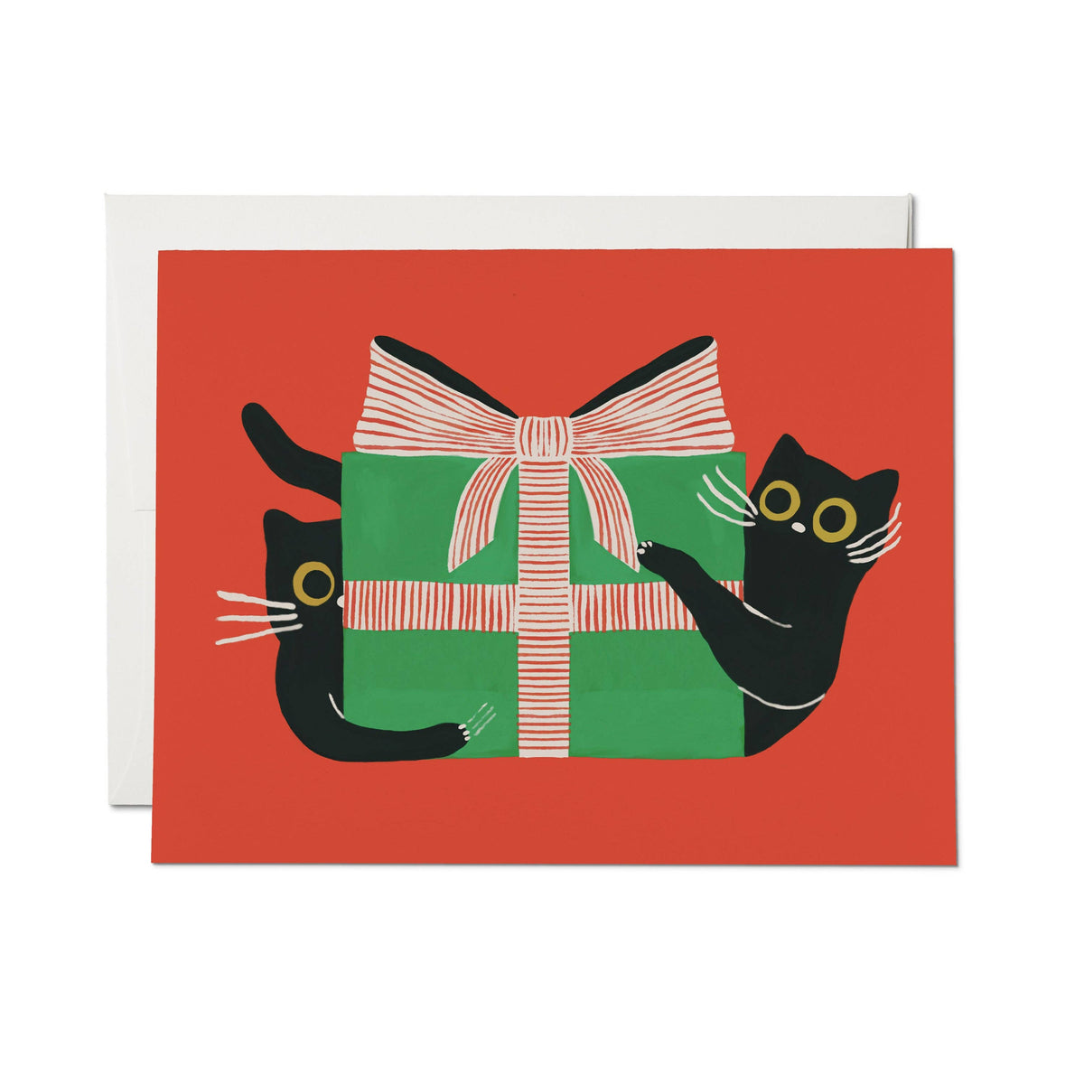 A greeting card with a red background featuring a black cat on each side of a green gift box wrapped with a pink-and-white striped ribbon. A white envelope is placed behind the card on a white background.