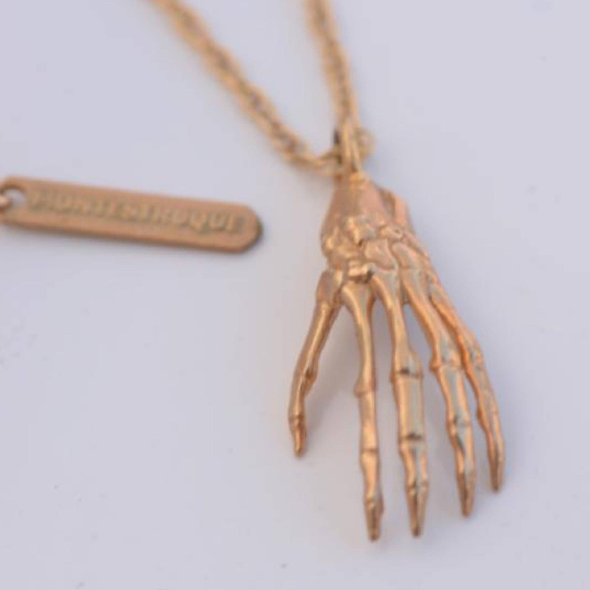 Gold skeleton hand necklace on a light gray background