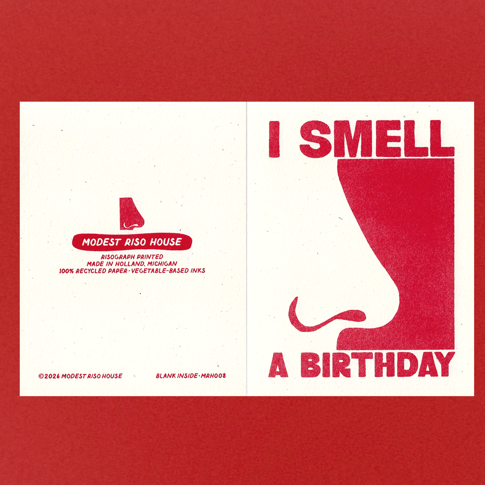 A square greeting card or print shown flat against a red background, featuring a white center panel with red text reading 'I SMELL A BIRTHDAY' and a large stylized red nose graphic. The left side includes small Modest Rise House branding and production text.