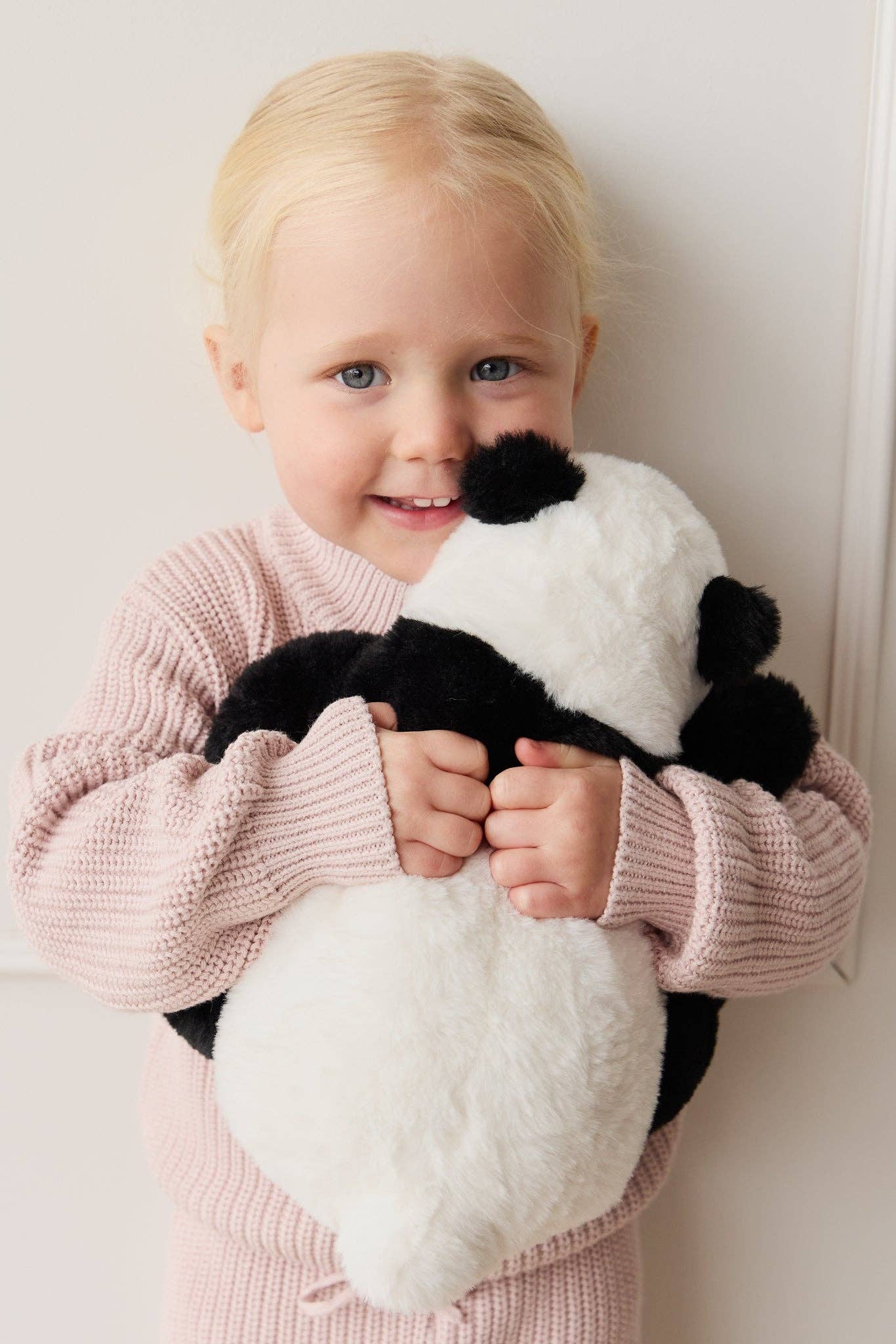 Child holding a panda plush toy against a white background