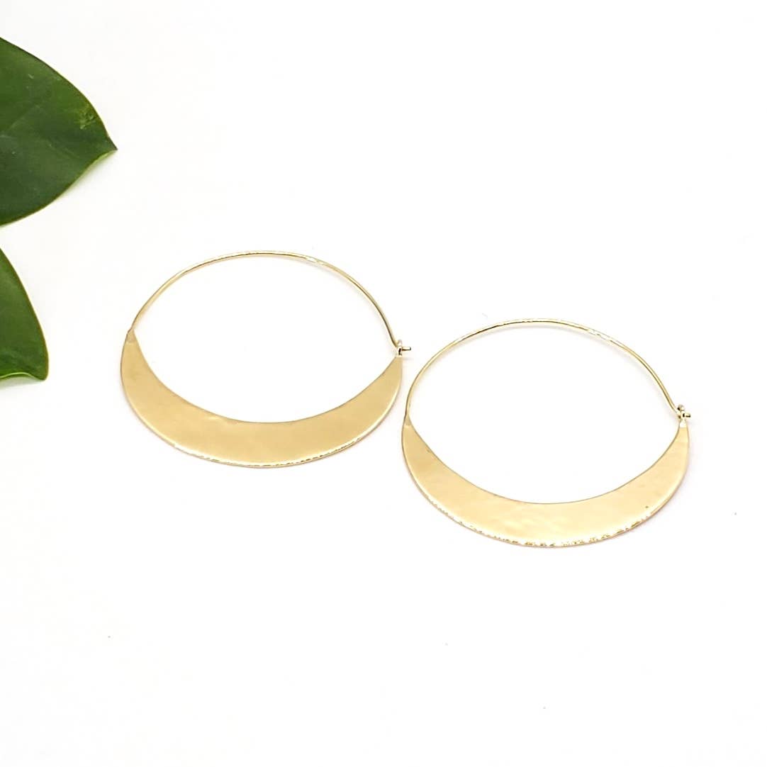 Gold hoop earrings on a white background with a green leaf