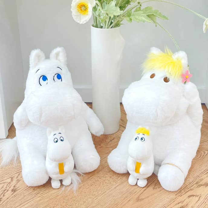 Two white plush toys resembling cartoon characters on a wooden floor with a vase and flowers in the background.
