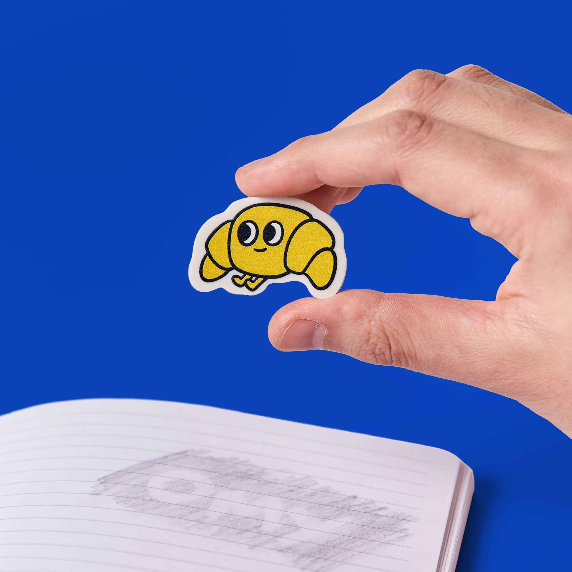 Hand holding a yellow cartoon character sticker above an open notebook with a blue background