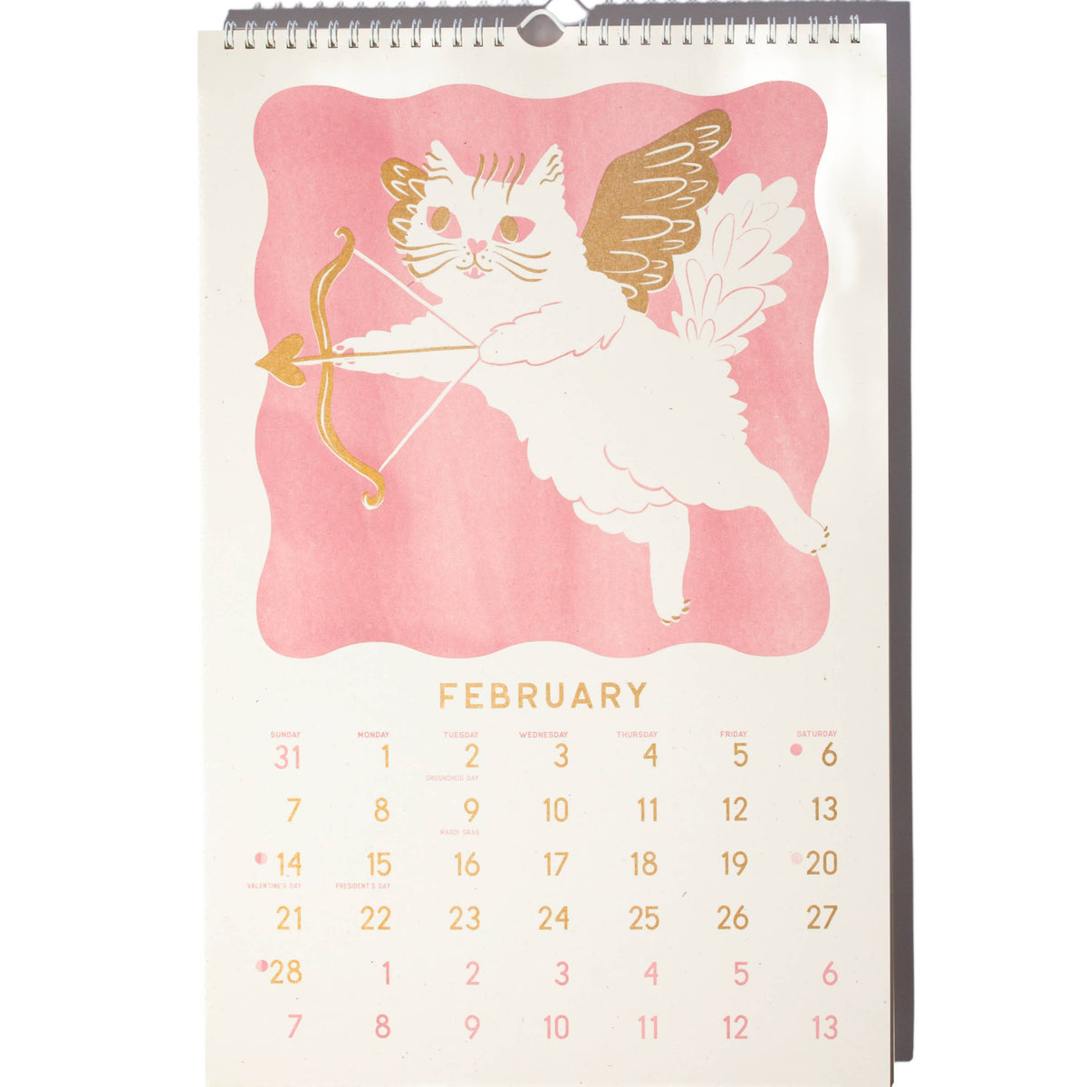 A spiral-bound February desk calendar featuring a pink watercolor background with a white angel cat holding a gold bow and arrow. The calendar page is cream-colored with gold text and dates, and is photographed against a plain white background.