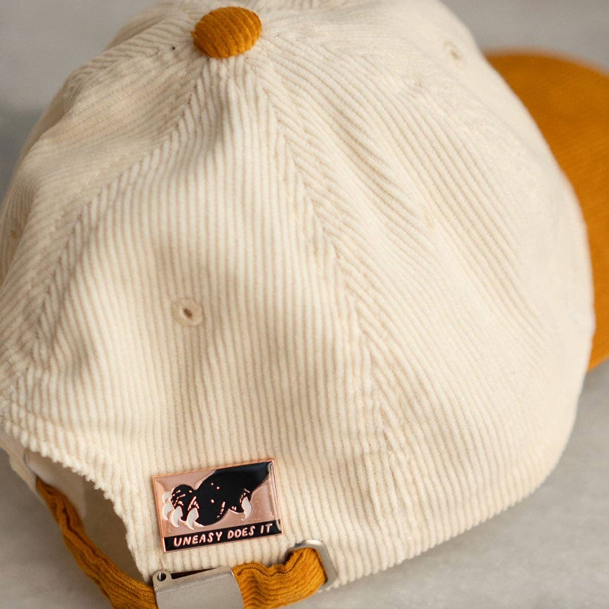 Beige cap with brown brim and patch on a gray surface