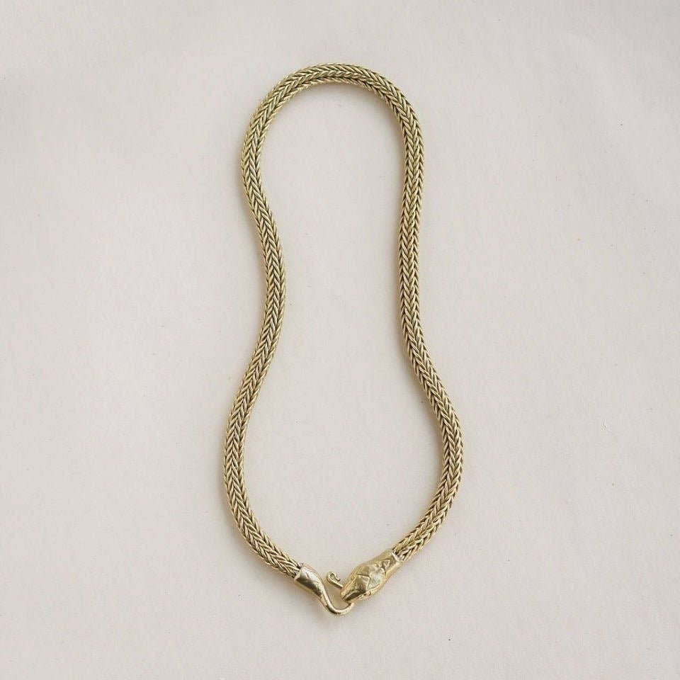 A gold-colored braided chain necklace with a lobster clasp, laid flat on a light off-white background.