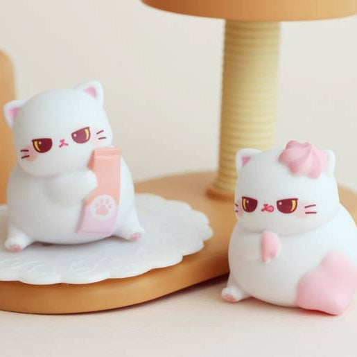 Two cute cat-shaped plush toys on a wooden surface with a neutral background