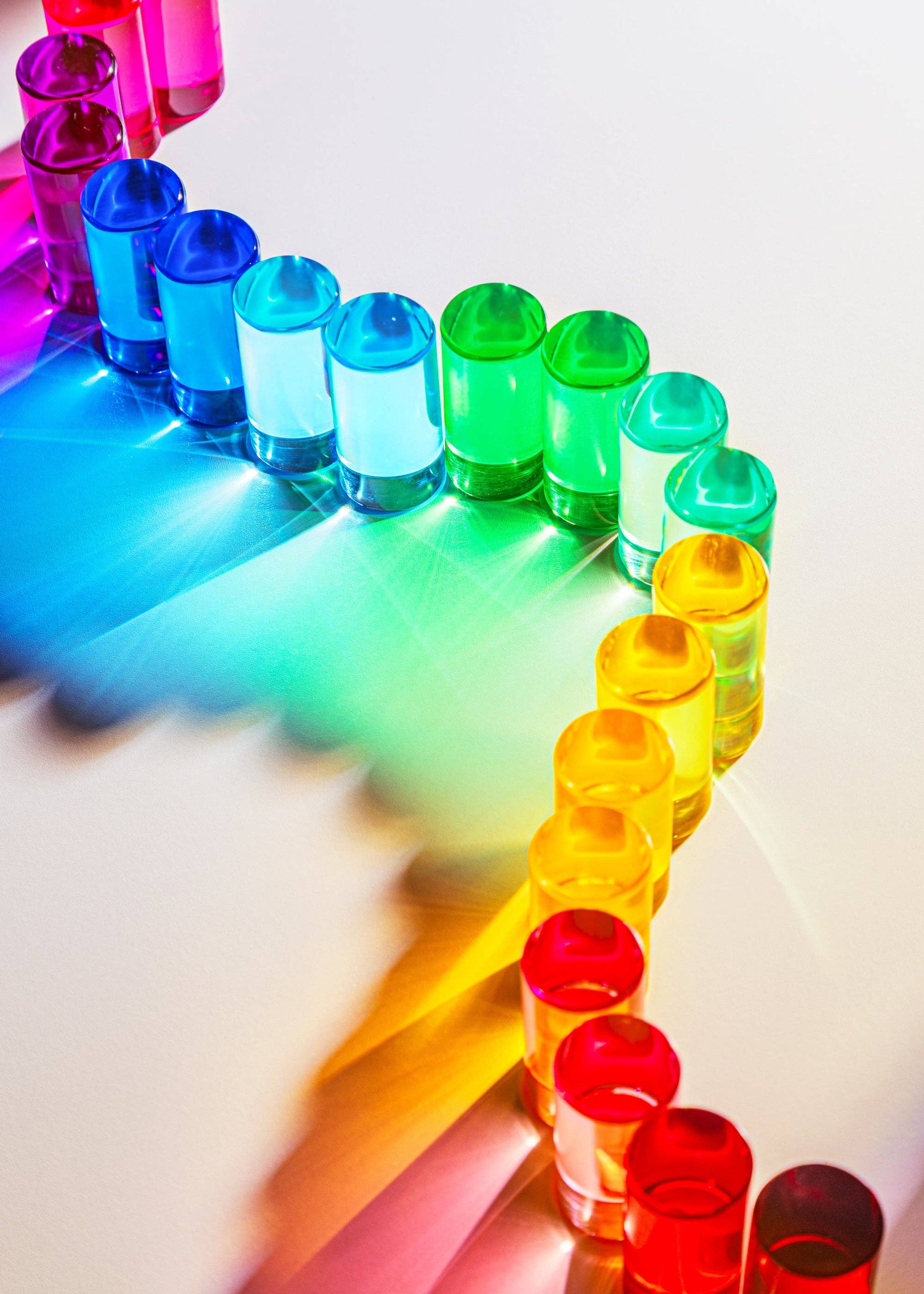 Colorful plastic cups arranged in a rainbow pattern on a reflective surface.