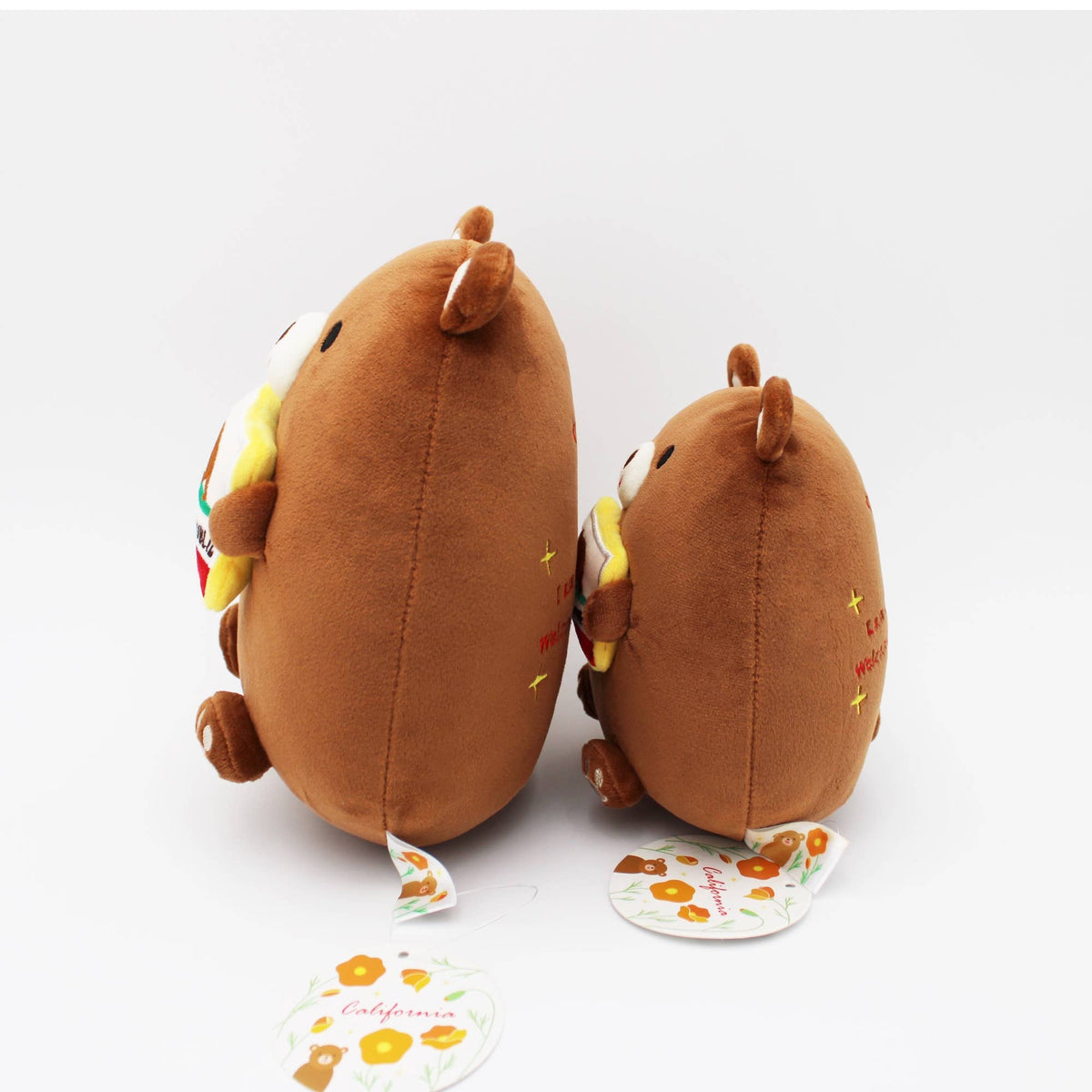 Two brown plush animal toys shaped like California coasters, shown from the back on a white background, with one toy showing a colorful side and the other showing embroidered details. Two small hang tags are in front.