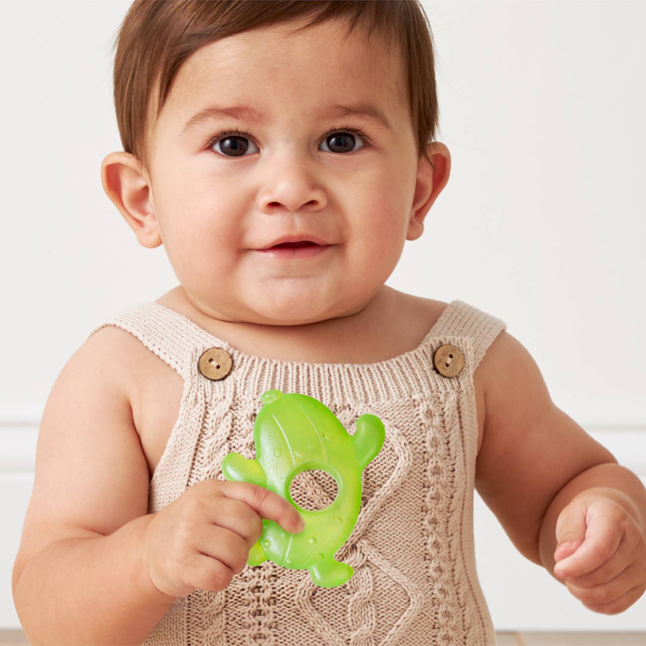 Baby holding a green teething toy against a white background
