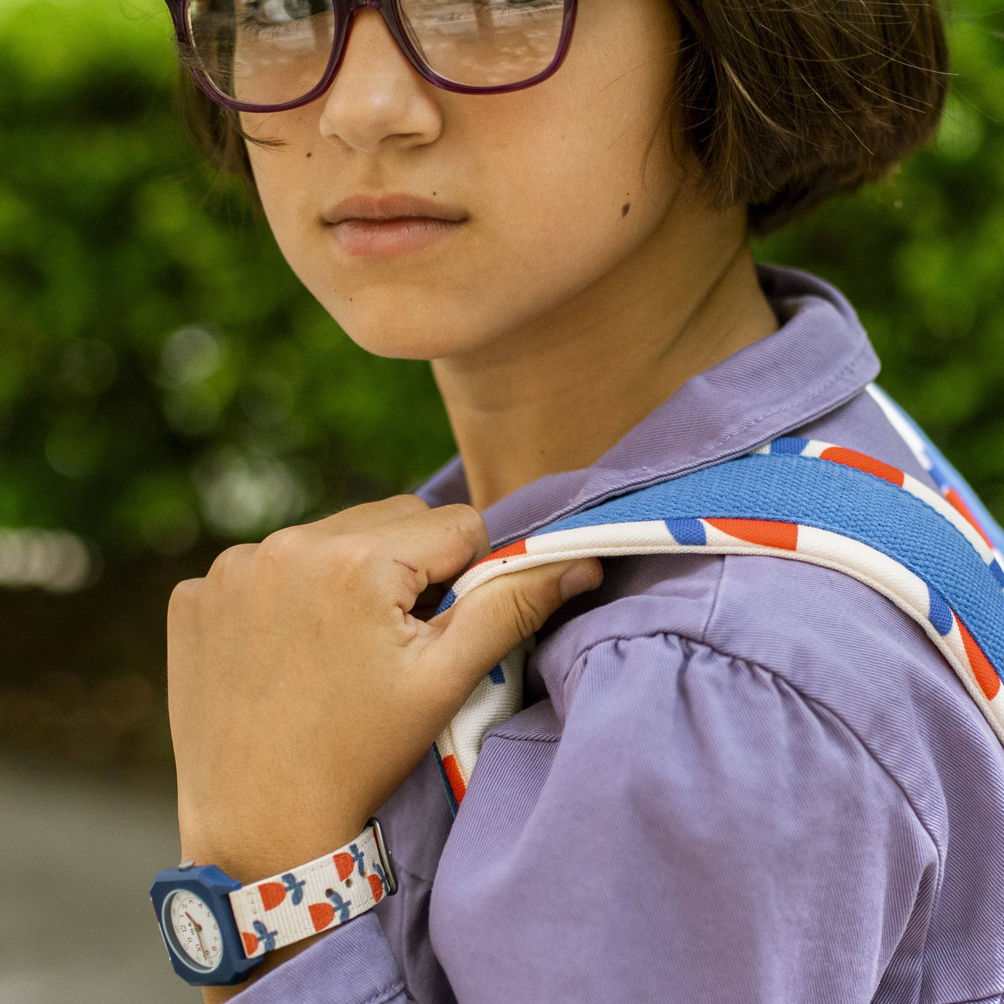 Person wearing a purple jacket with a colorful strap over their shoulder, outdoors.