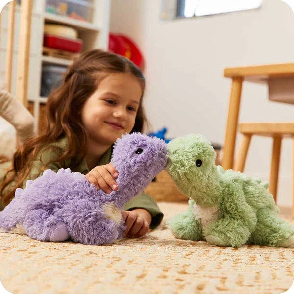 Child playing with two plush dinosaurs, a purple one and a green one, on a bed.
