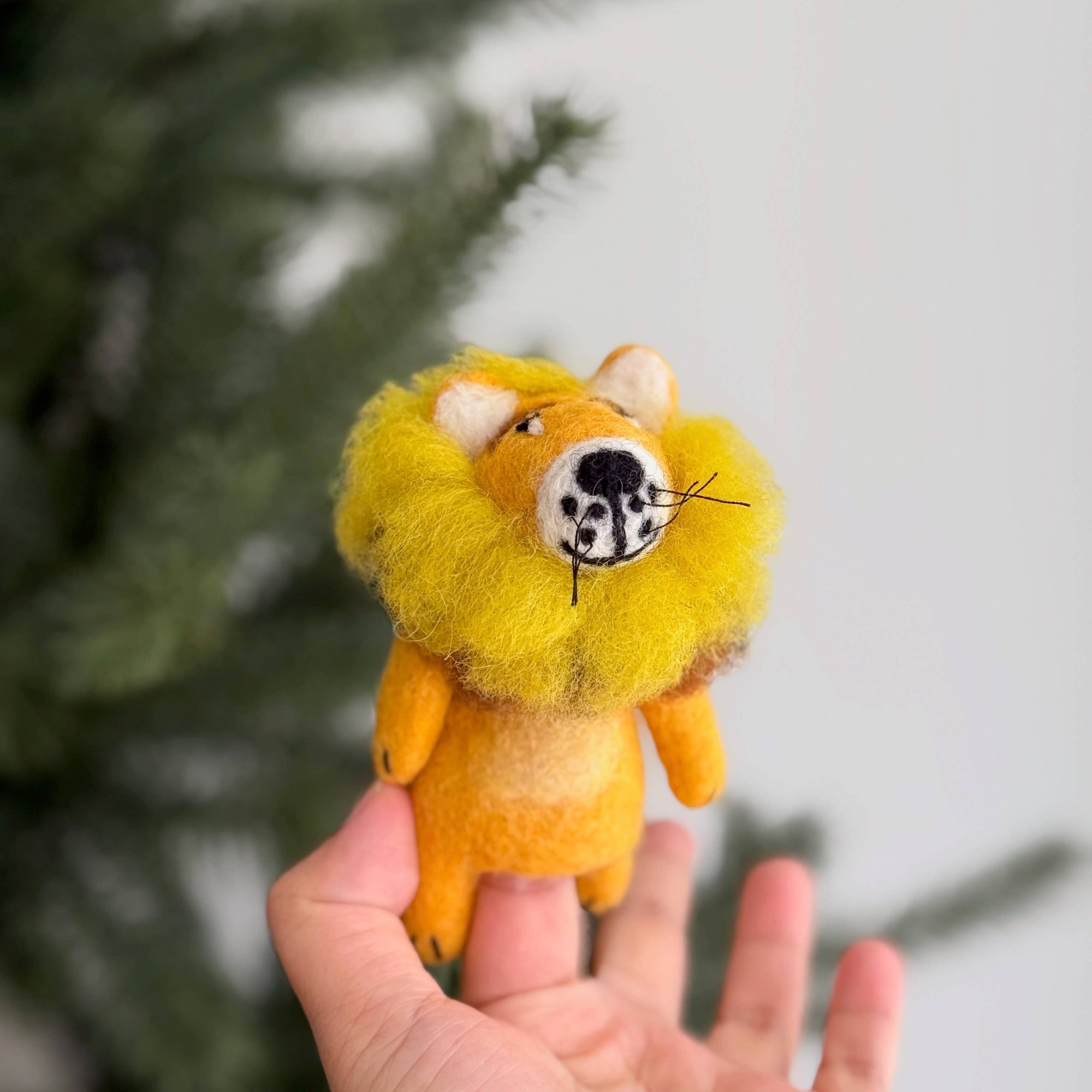 Hand holding a small lion plush toy with a blurred natural background