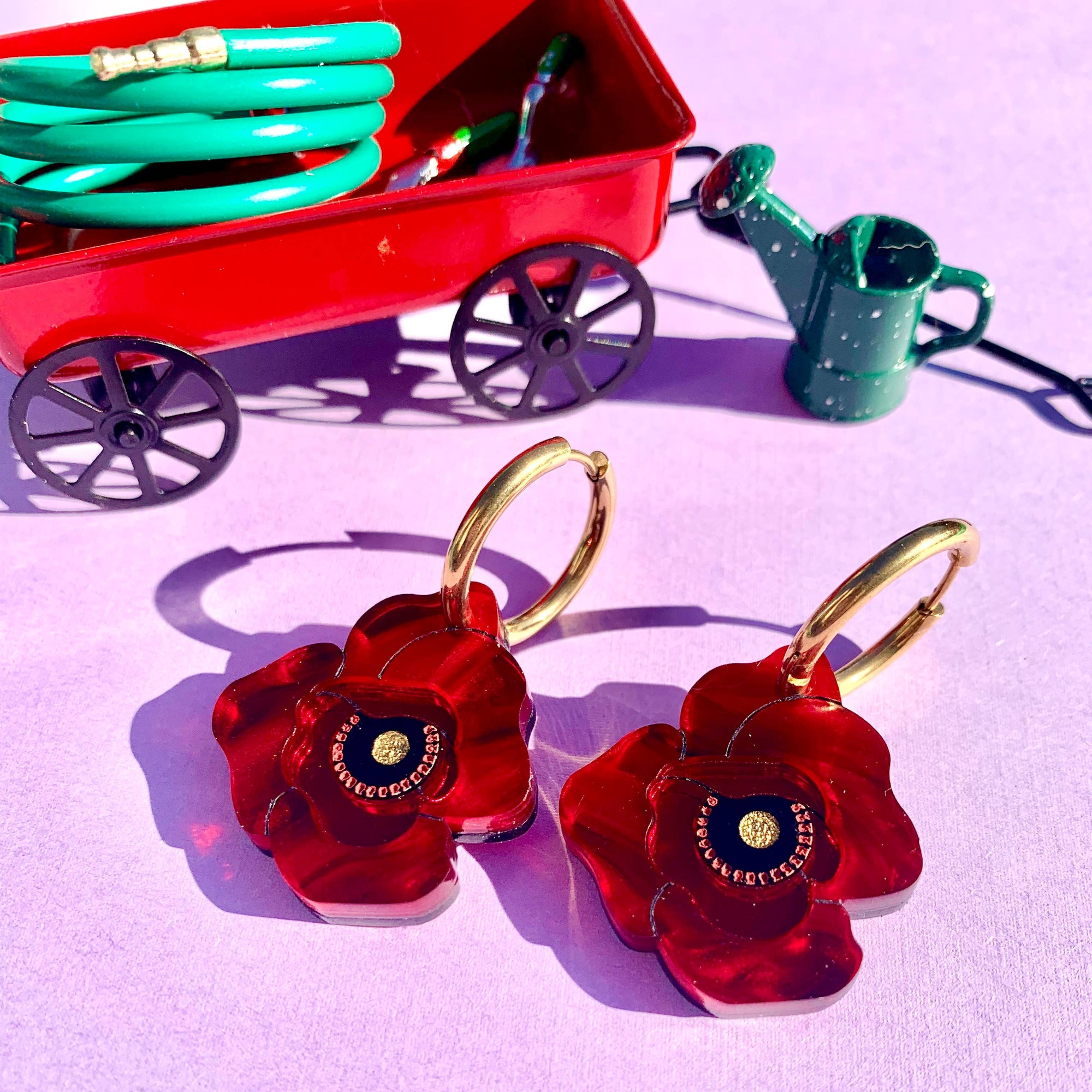 Red flower-shaped earrings with gold hooks on a pink background