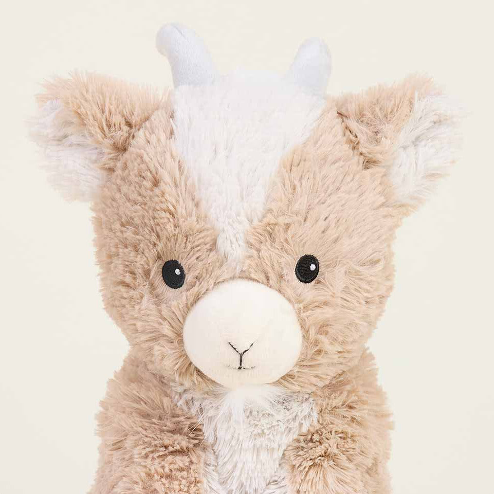 Plush toy resembling a creature with a brown body, white face, and gray horns on a beige background