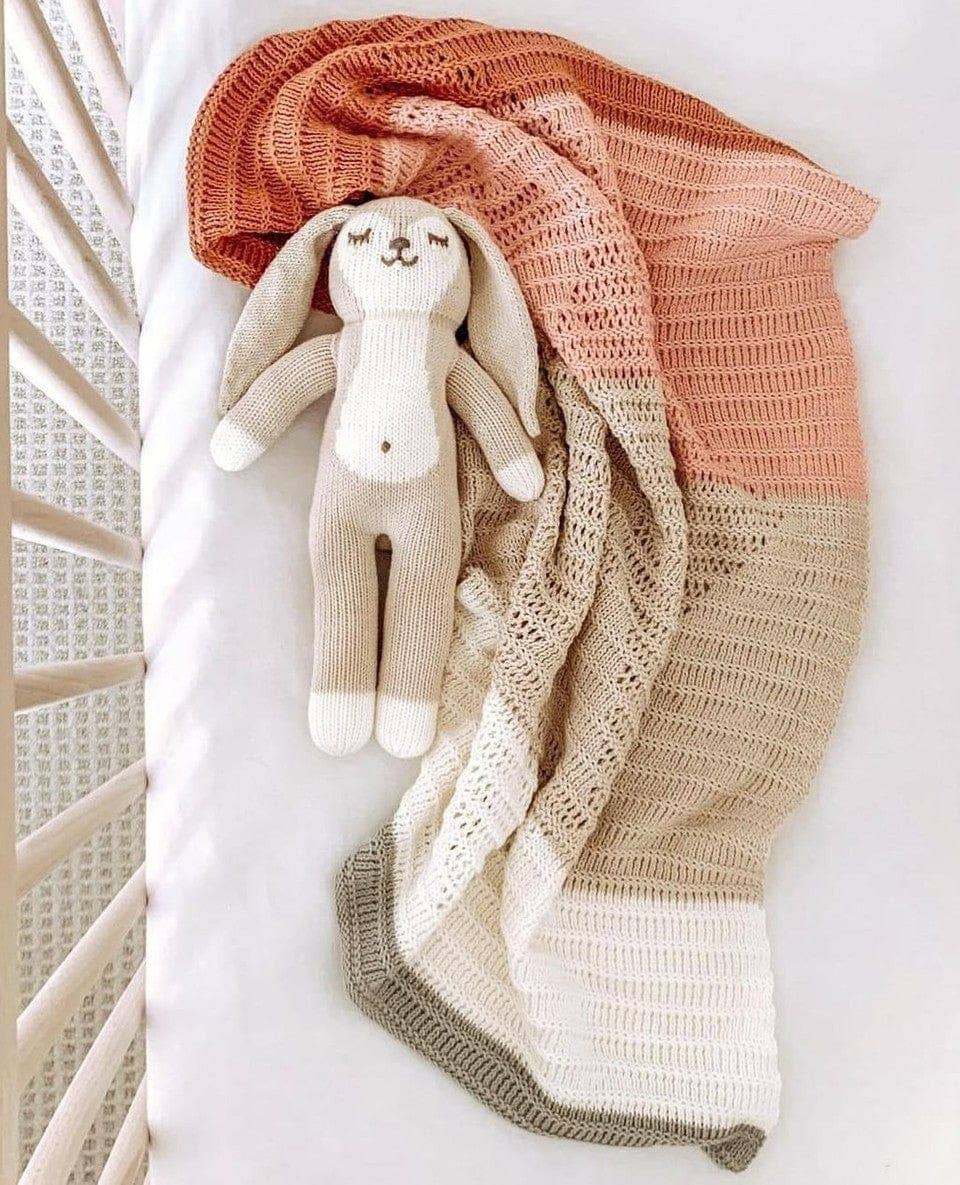 Knitted blanket with a bunny toy draped over it on a white surface.