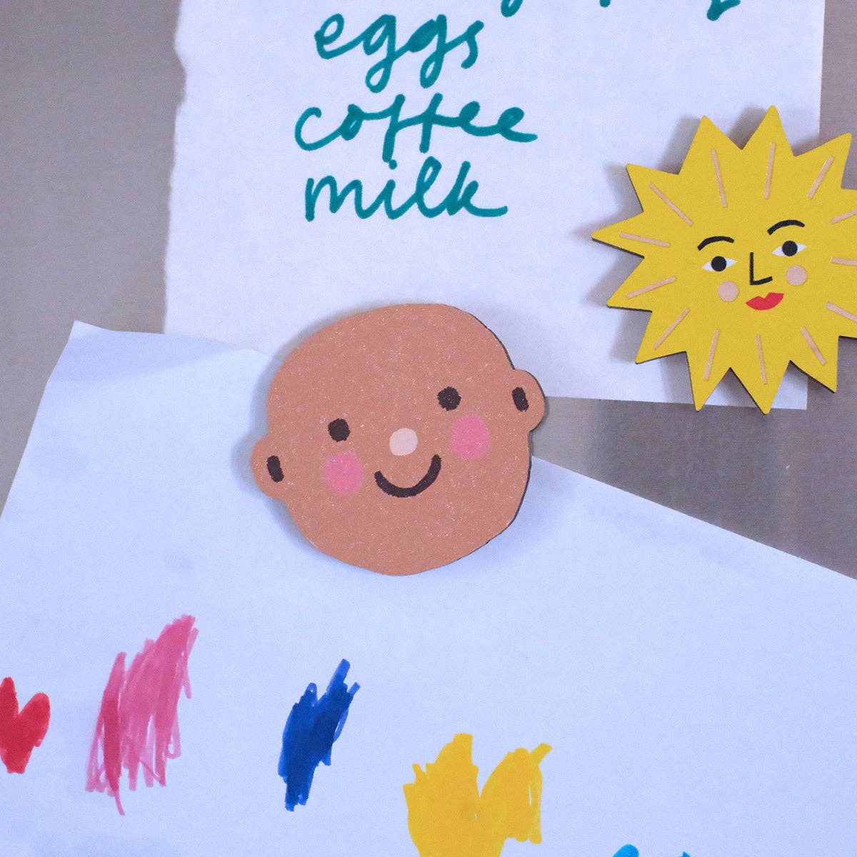 Children's craft project with a face cutout, colored shapes, and a sun decoration on a white background.