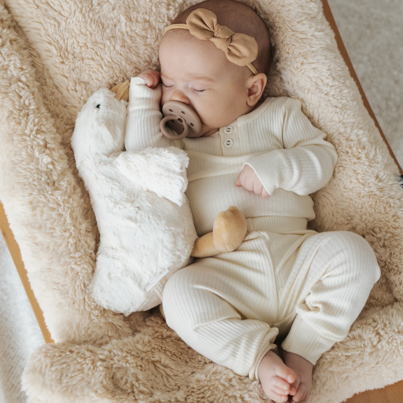 Baby in a white onesie with a teddy bear on a soft surface