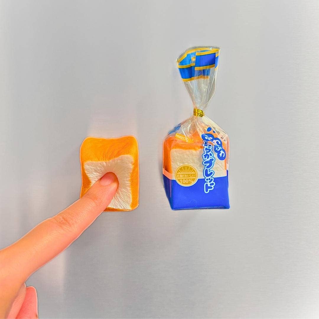 Hand holding a small square of food next to a larger package on a gray background
