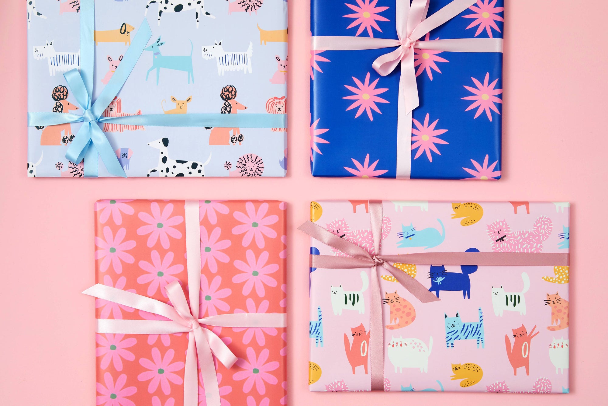 Four wrapped gifts with colorful patterns and ribbons on a pink background