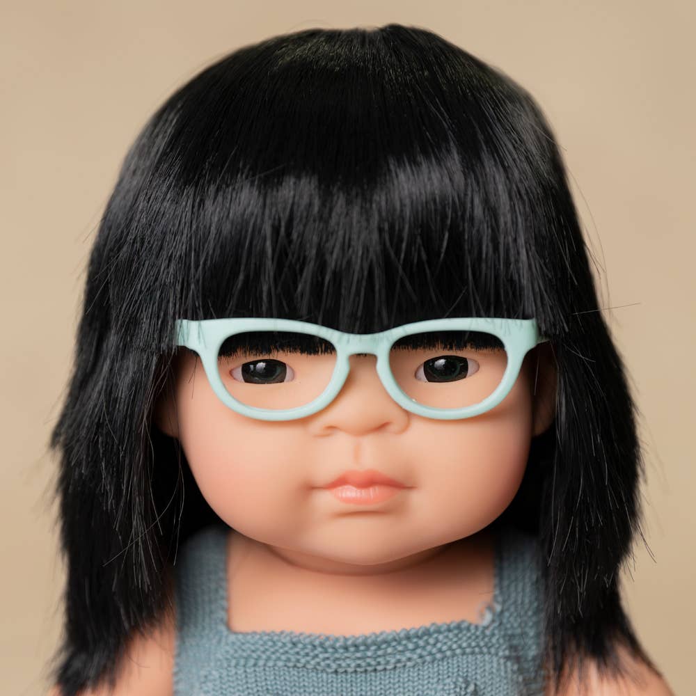 Doll with black hair and light blue glasses on a beige background