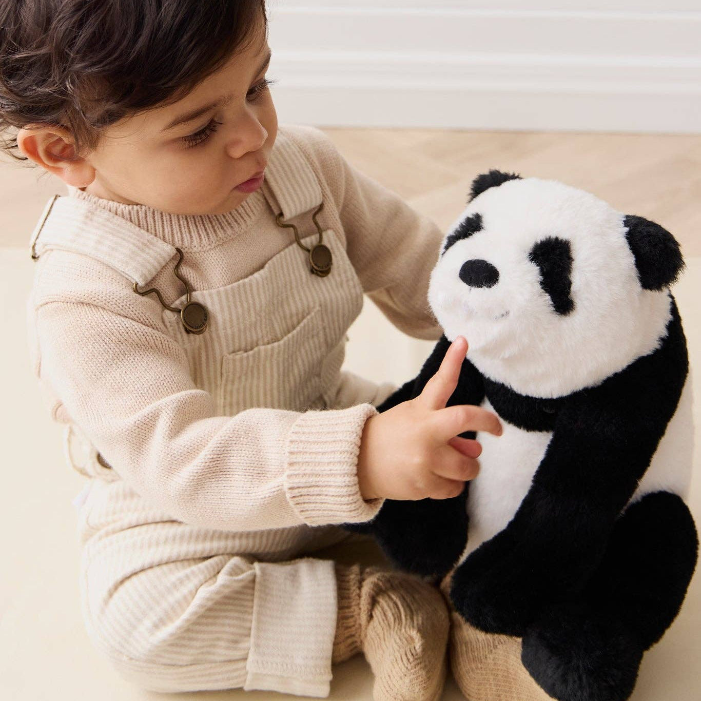 Child holding a plush panda toy on a light-colored couch