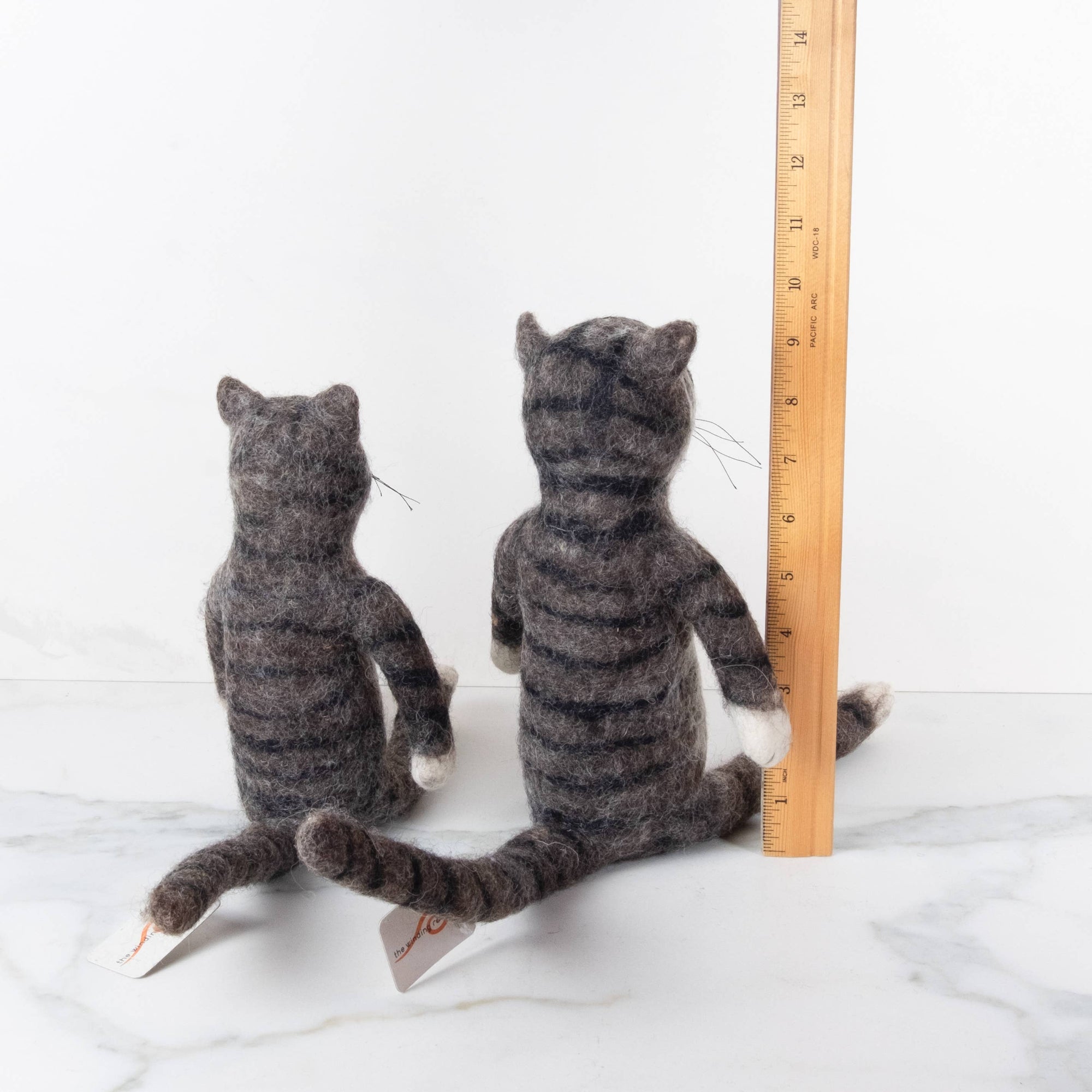 Two needle-felted cats next to a wooden ruler on a white background