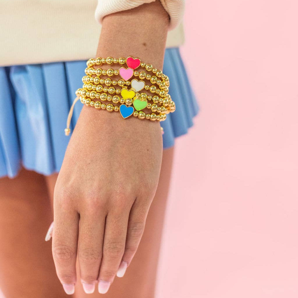 Gold beaded bracelet with colorful beads on a wrist against a pink background