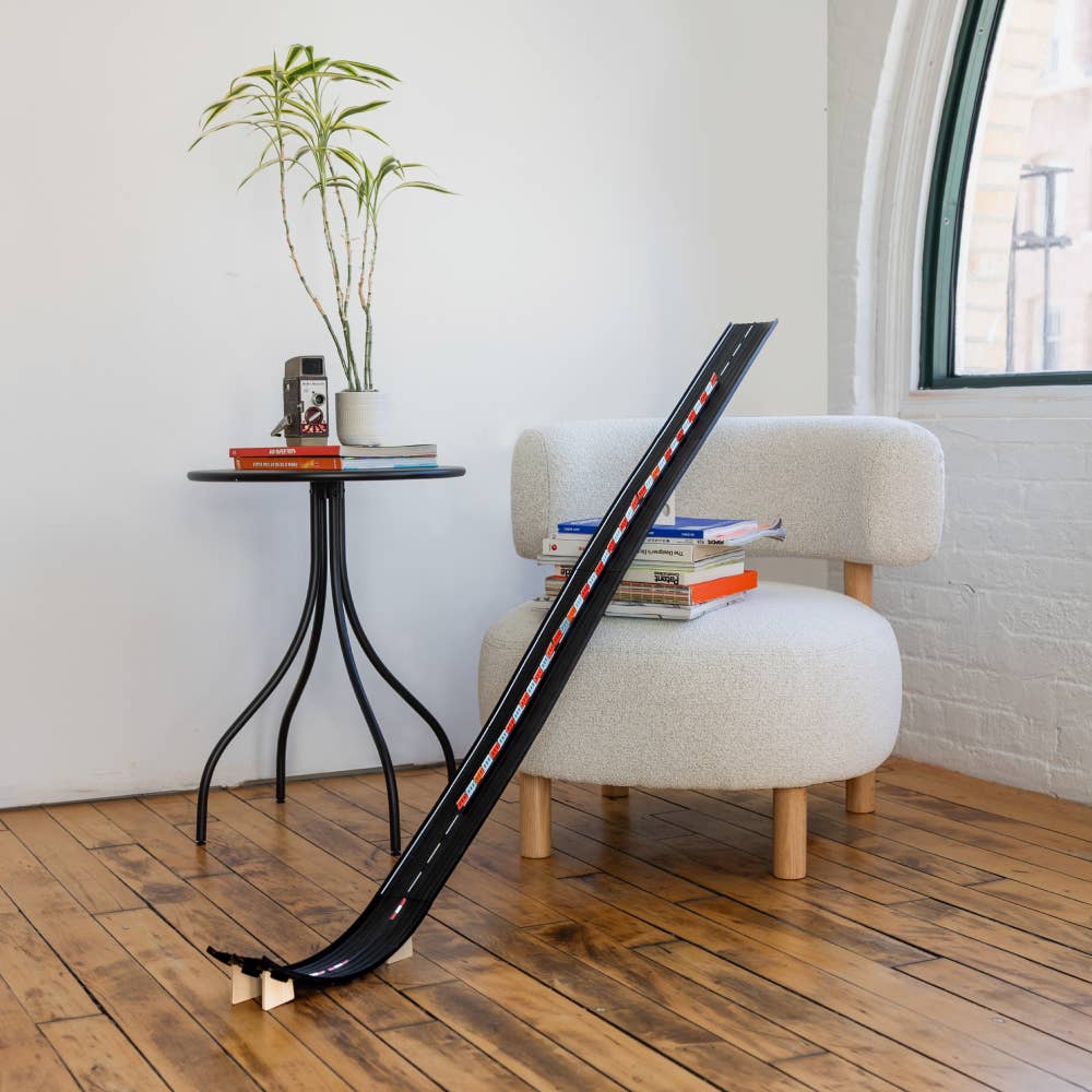 Black lacrosse stick leaning against a white chair with a plant and books on a small table in the background.