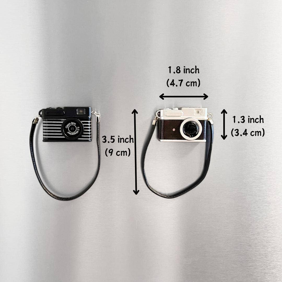 Two camera-shaped keychains with measurements on a gray background