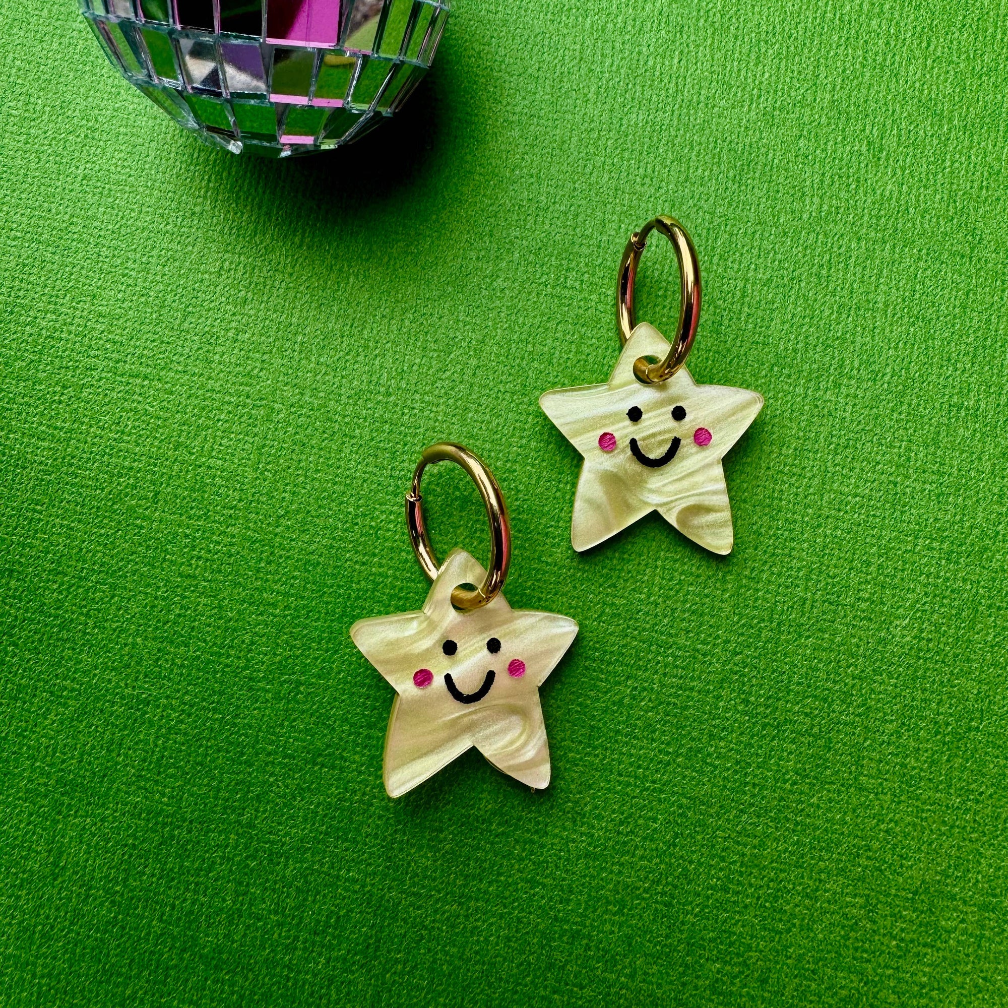 Two star-shaped charms with smiley faces on a green background with a disco ball.