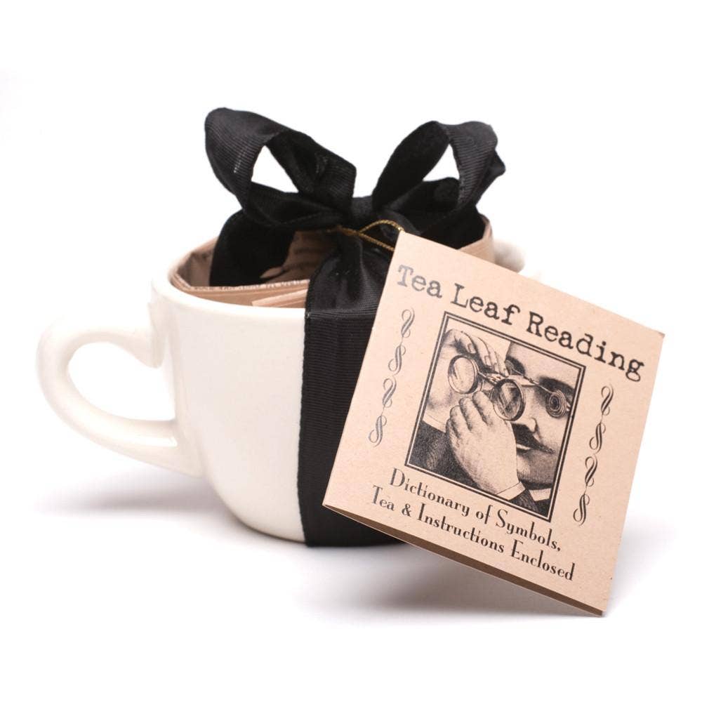 White mug with black ribbon and 'Tea Leaf Reading' book on a white background