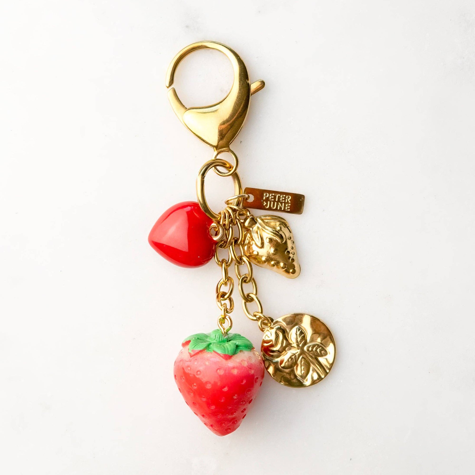Gold keychain with strawberry and heart charms on a white background