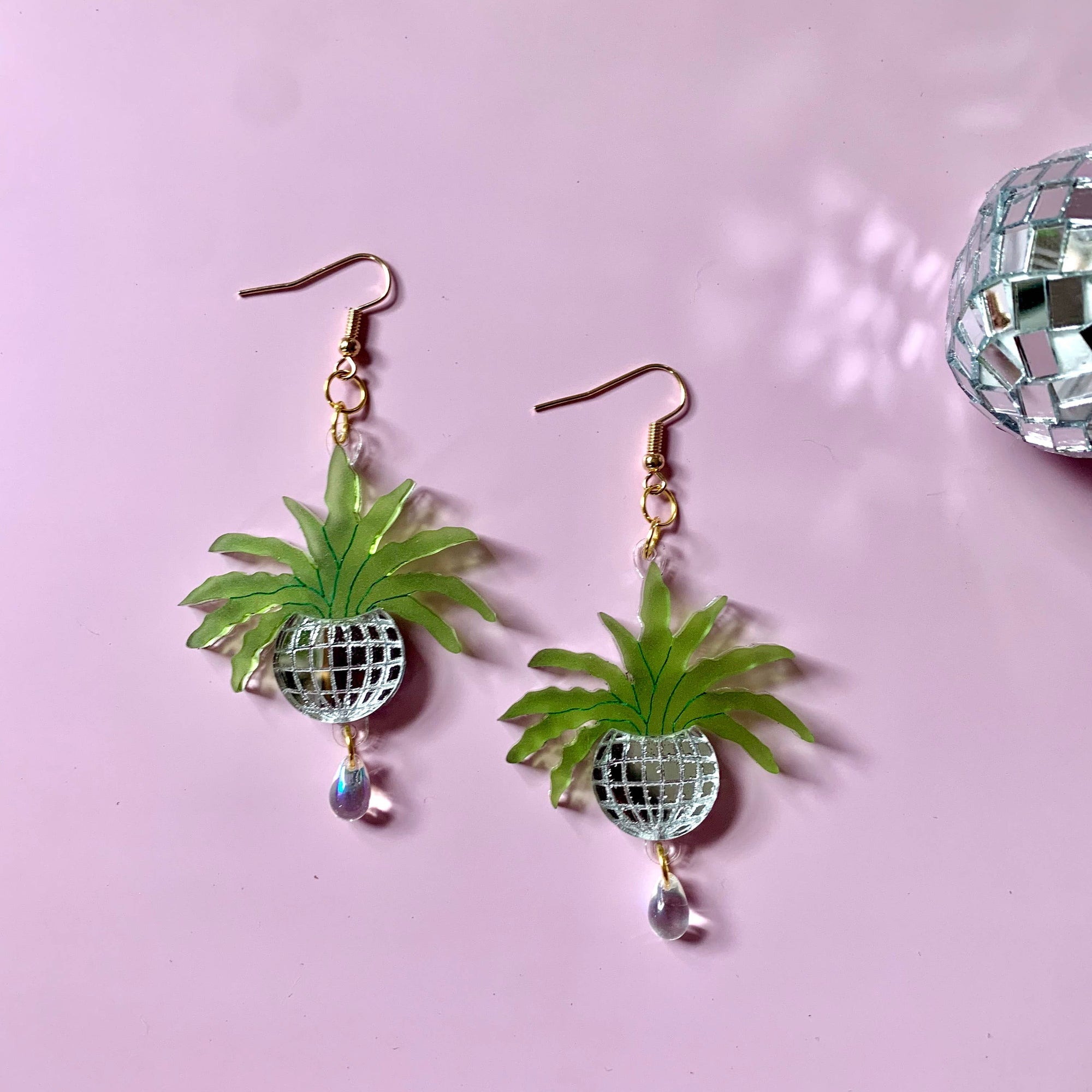Pineapple-shaped earrings with green leaves and clear gemstones on a pink background