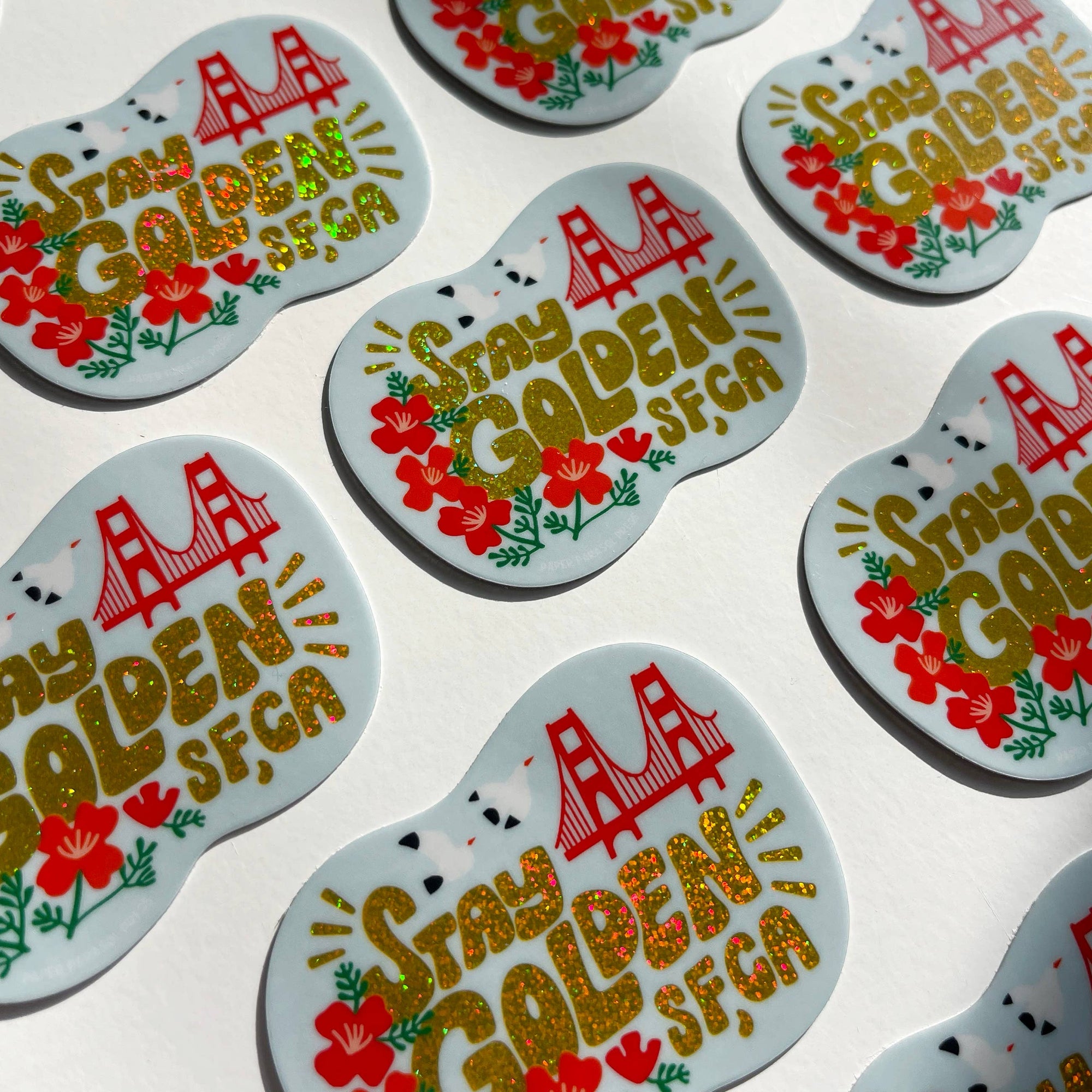 Stickers with 'Stay Golden SFG' text and floral designs on a light background